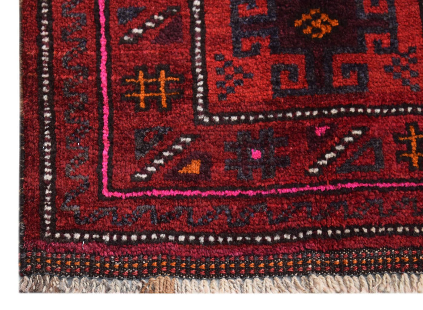 A close-up of a vintage Afghan Baluch rug featuring geometric patterns in deep red and dark blue.