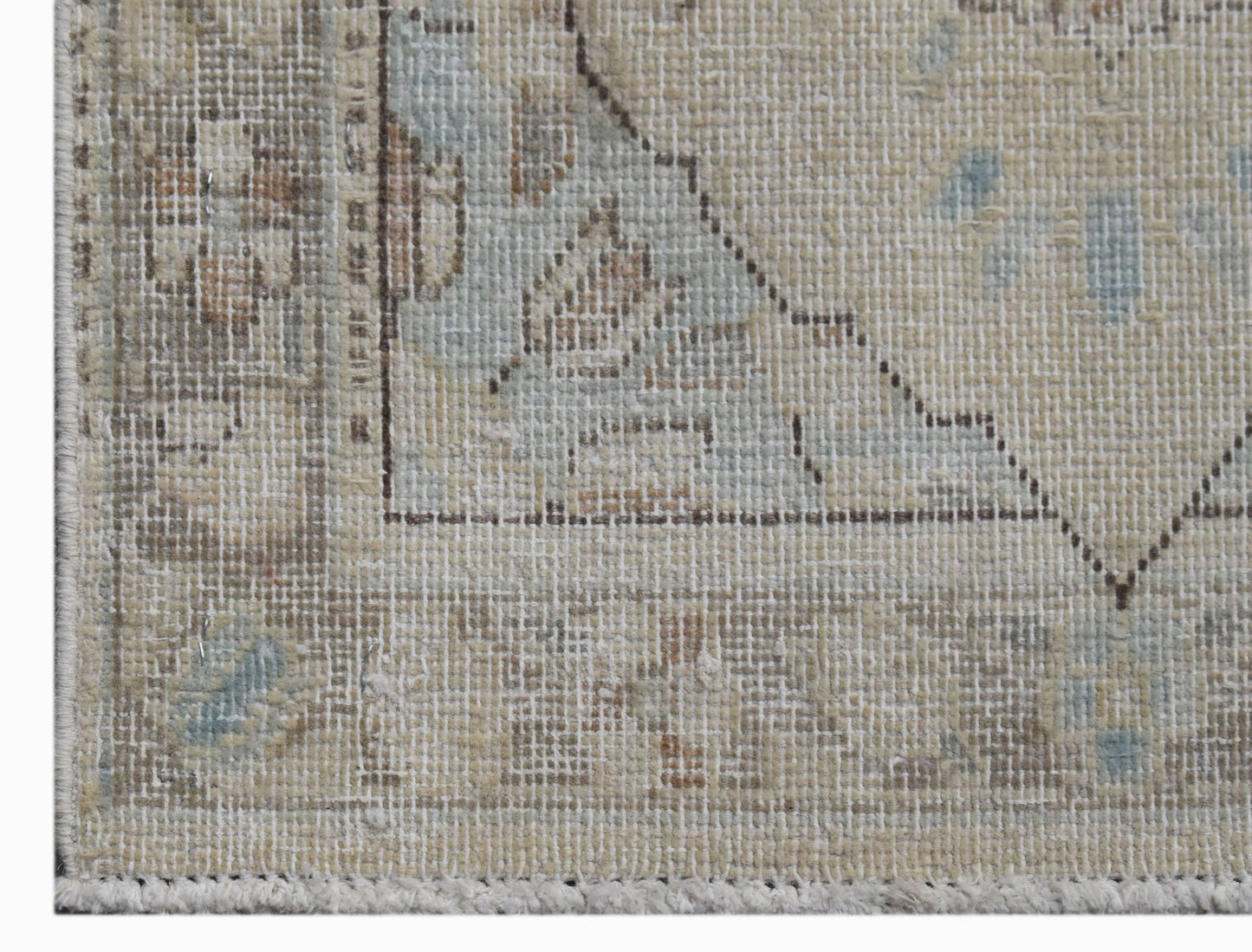 A close-up of a vintage Persian Kerman rug featuring a faded floral medallion and neutral tones.