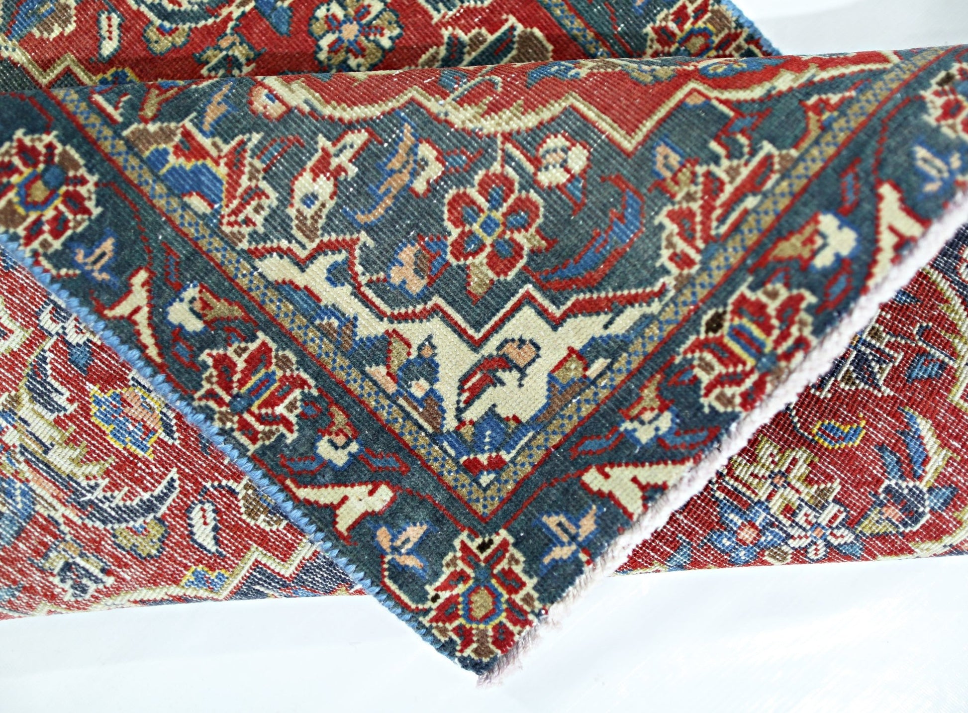 A folded vintage Persian rug featuring intricate floral patterns in red, blue, and cream tones.
