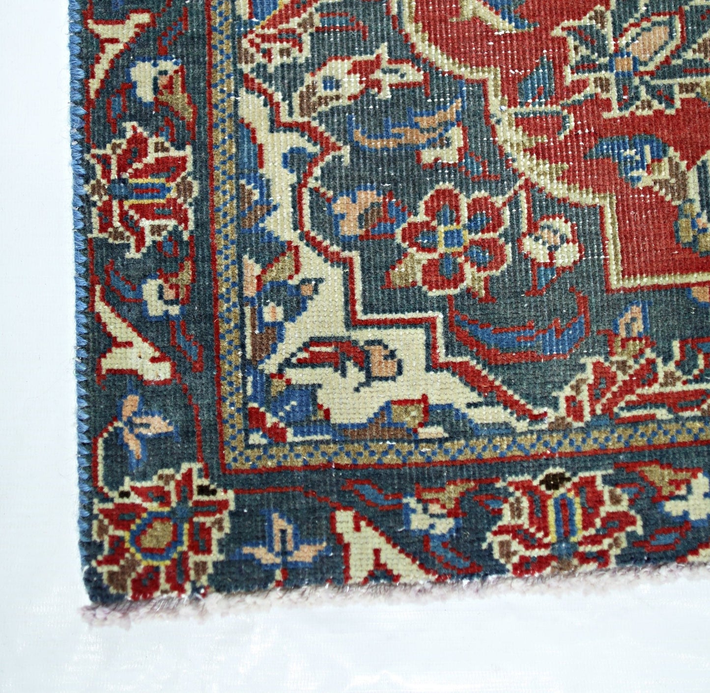 A corner view of a handmade vintage Persian rug featuring intricate floral patterns in red and blue.