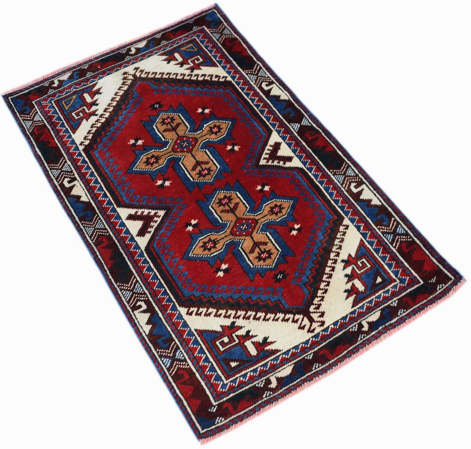 A handwoven vintage Turkish rug featuring a red central field with two tan cross-shaped motifs.