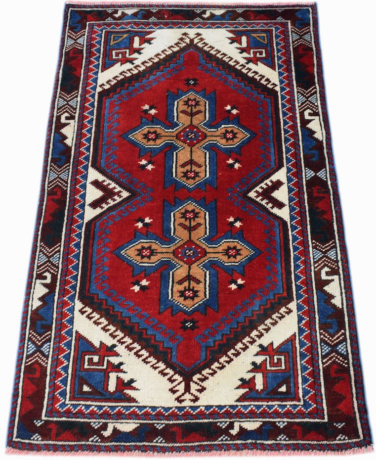 A handwoven vintage Turkish rug featuring a red field with two blue and tan cross motifs.