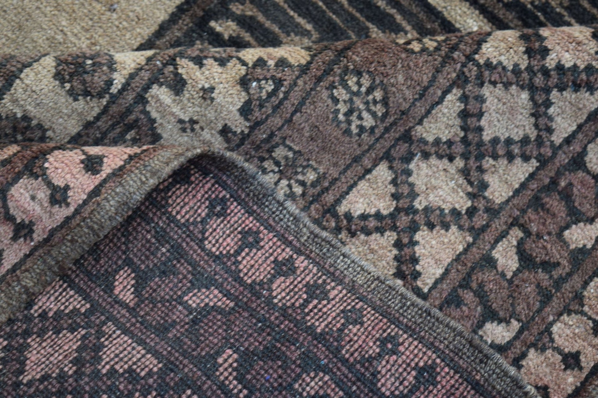 A close-up view of a vintage Afghan Turkmen rug showing its intricate geometric wool pattern.