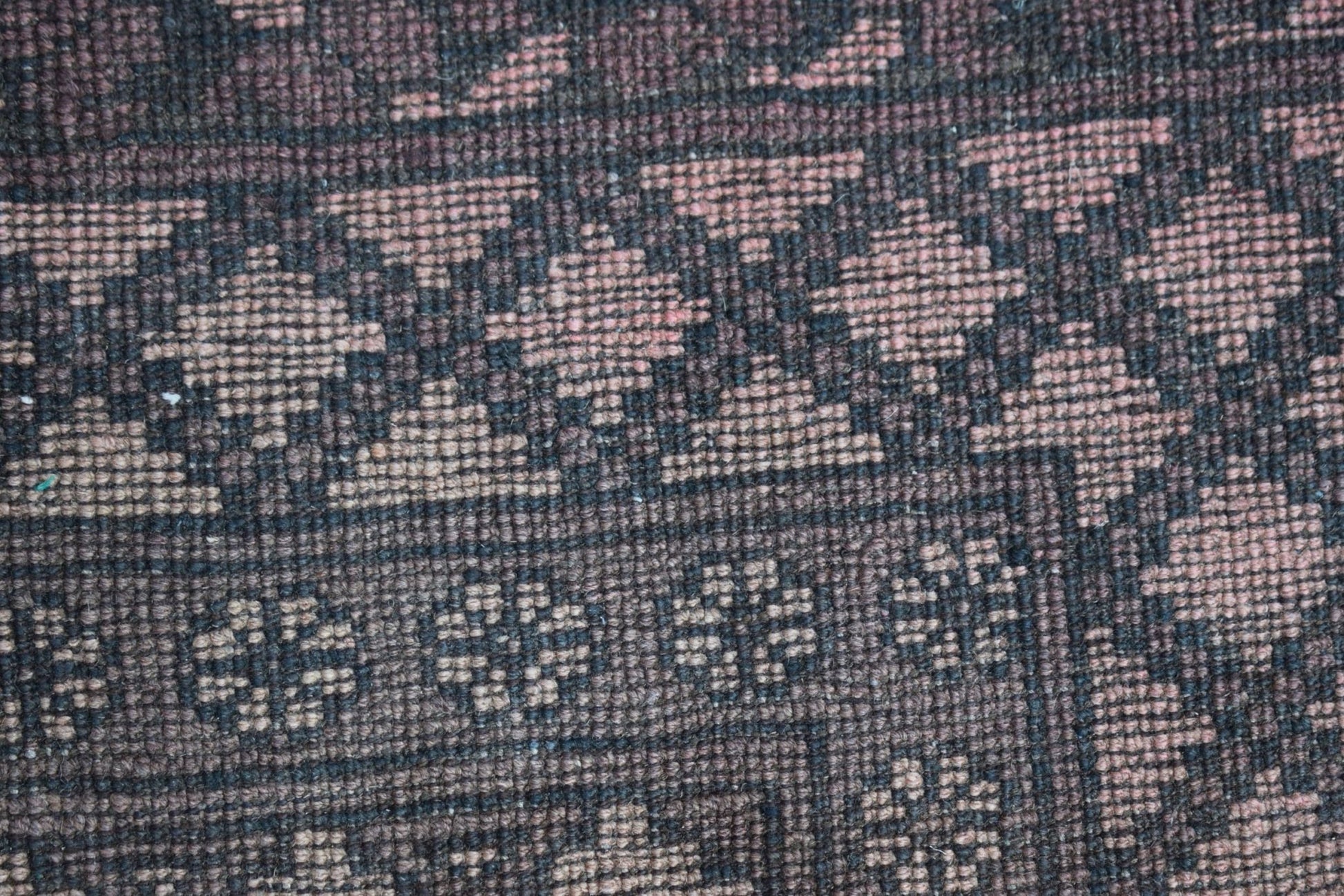 A close-up of a vintage Afghan Turkmen rug featuring geometric patterns in dark brown and tan wool.