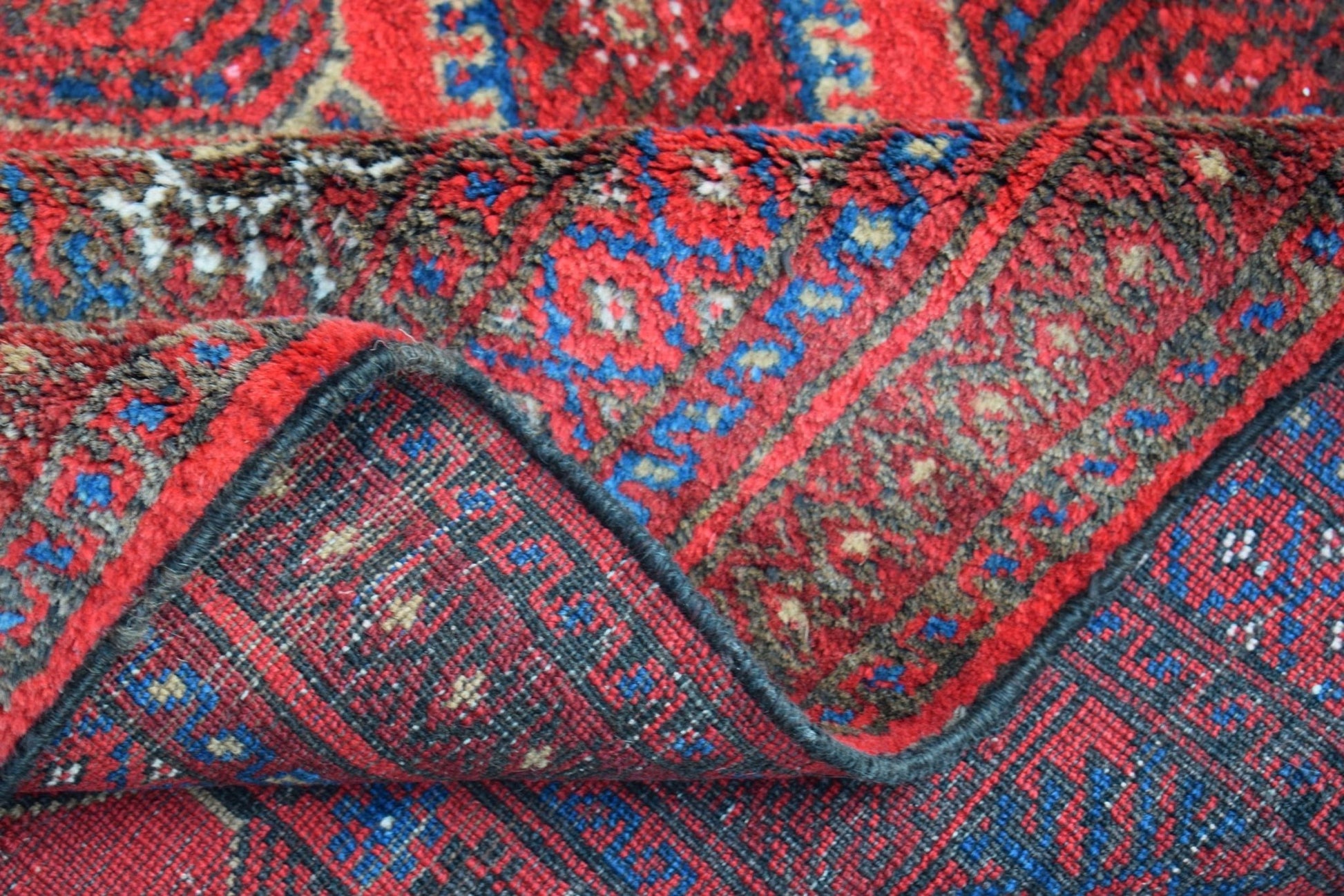 A vintage handmade Afghan Baluch wool rug featuring a geometric pattern in red and blue tones.