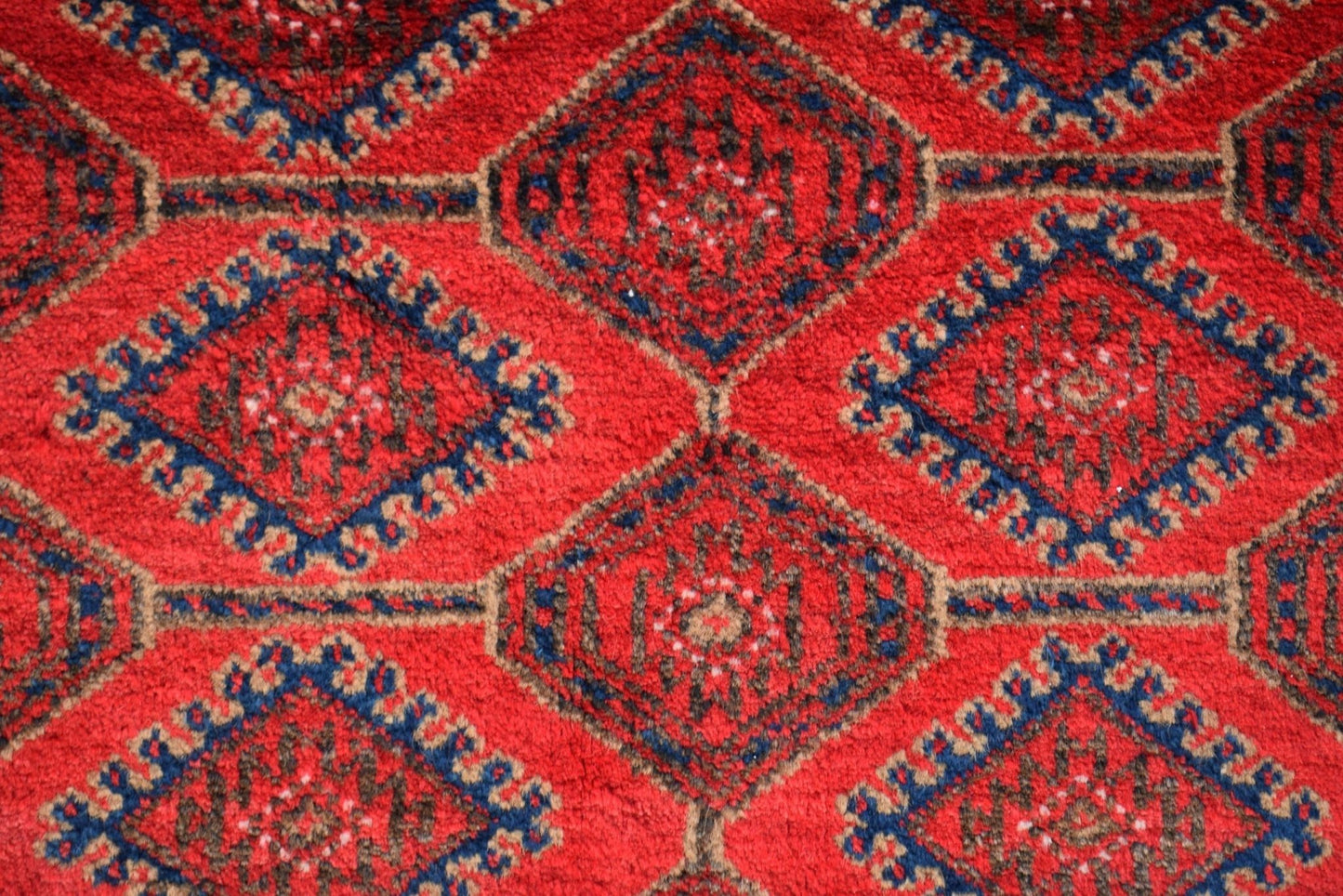 A vintage Afghan Baluch rug featuring a repeating diamond pattern in red, blue, and brown wool.