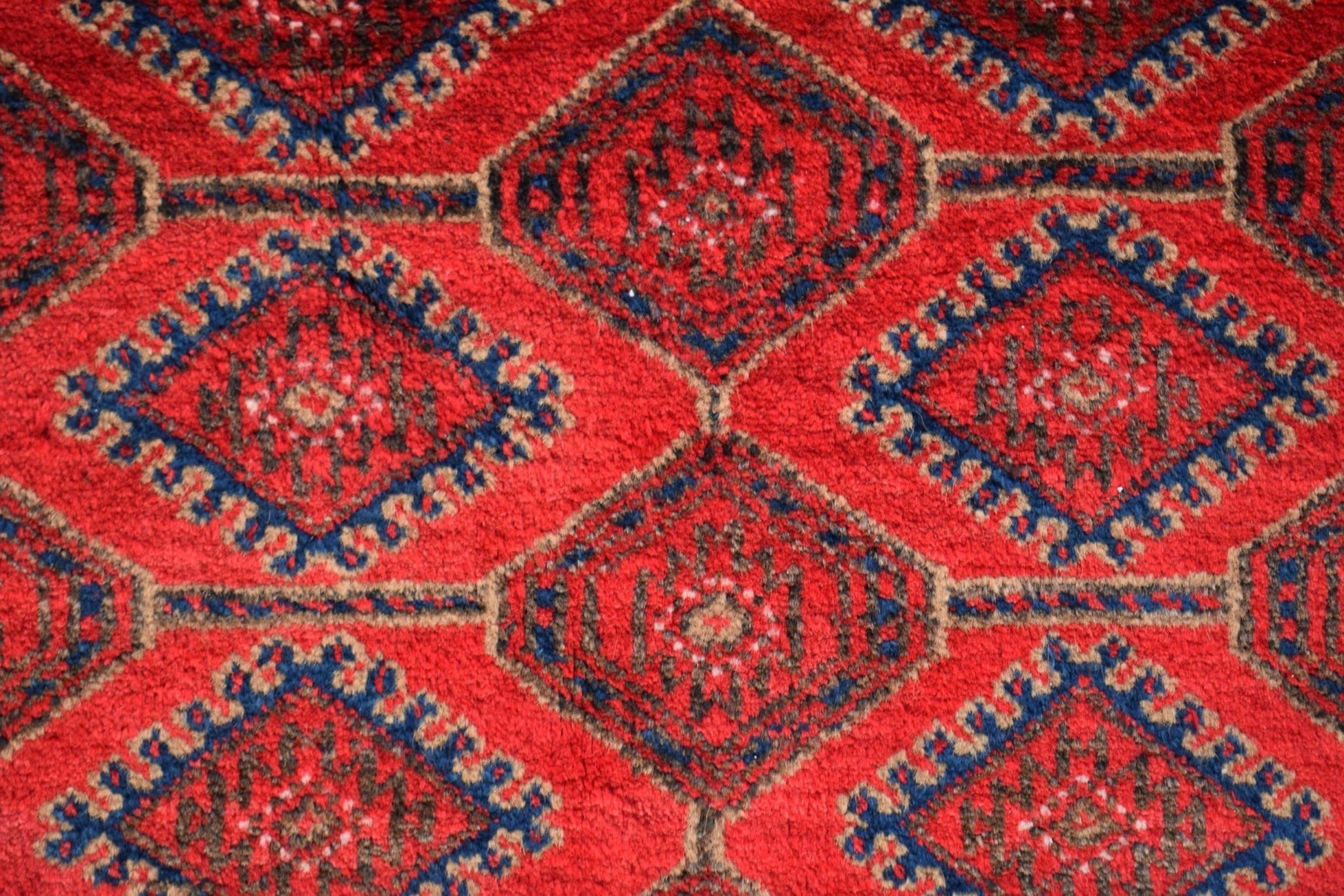 A vintage Afghan Baluch rug featuring a repeating diamond pattern in red, blue, and brown wool.