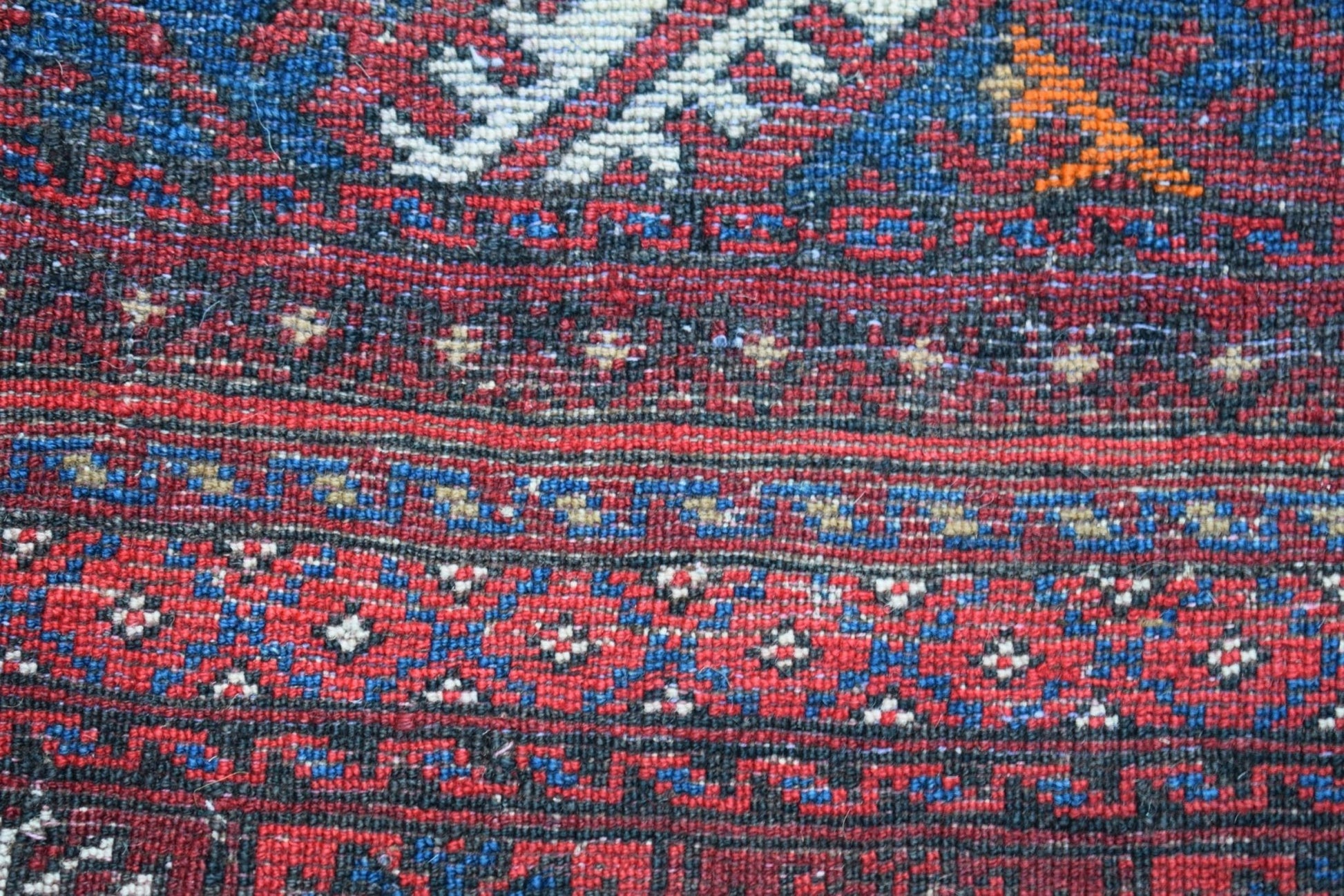 A close-up of a vintage Afghan Baluch wool rug featuring intricate geometric patterns in red and blue.