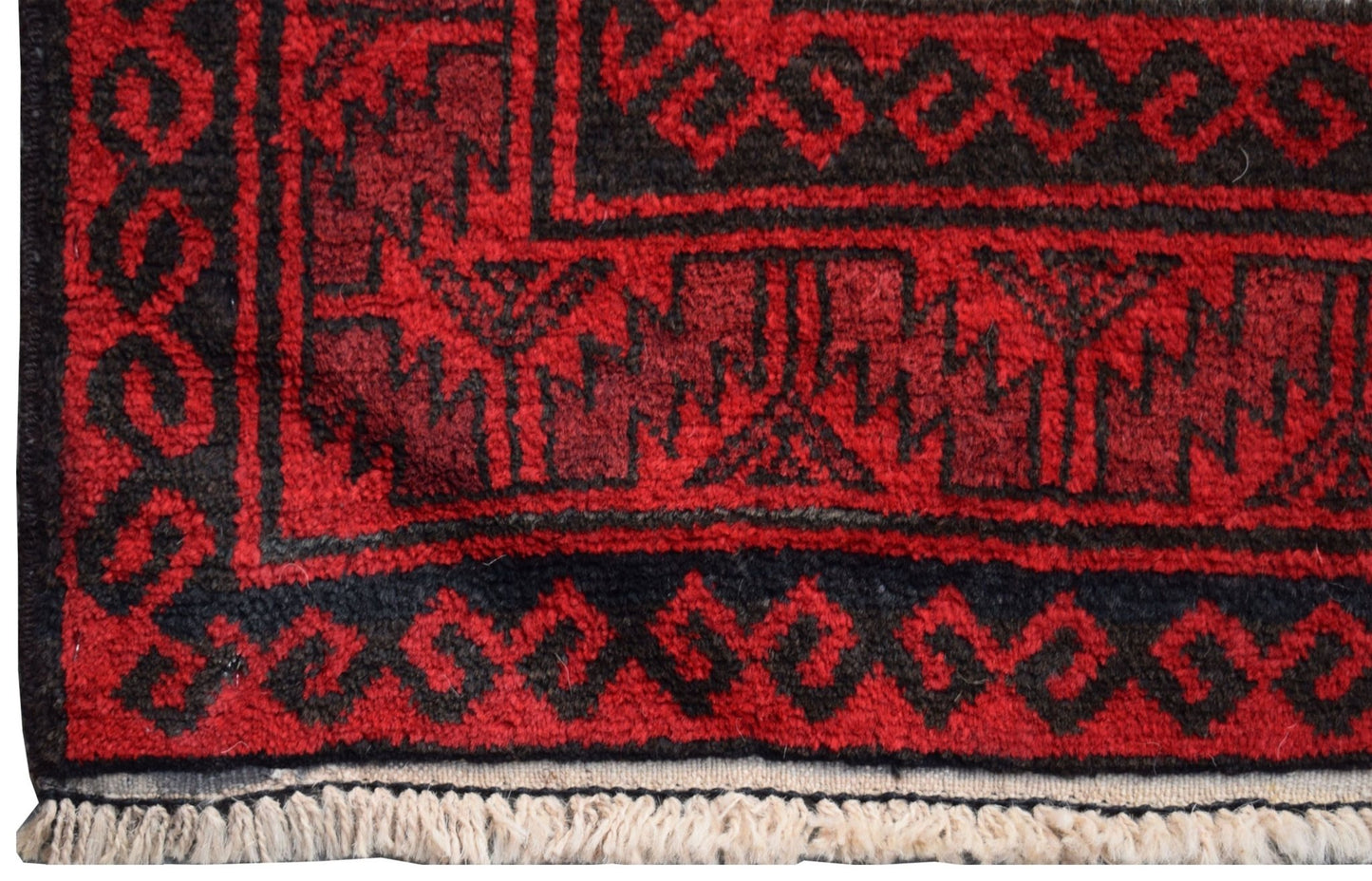 A close-up of a vintage Afghan Baluch rug featuring geometric black patterns on a red wool field.