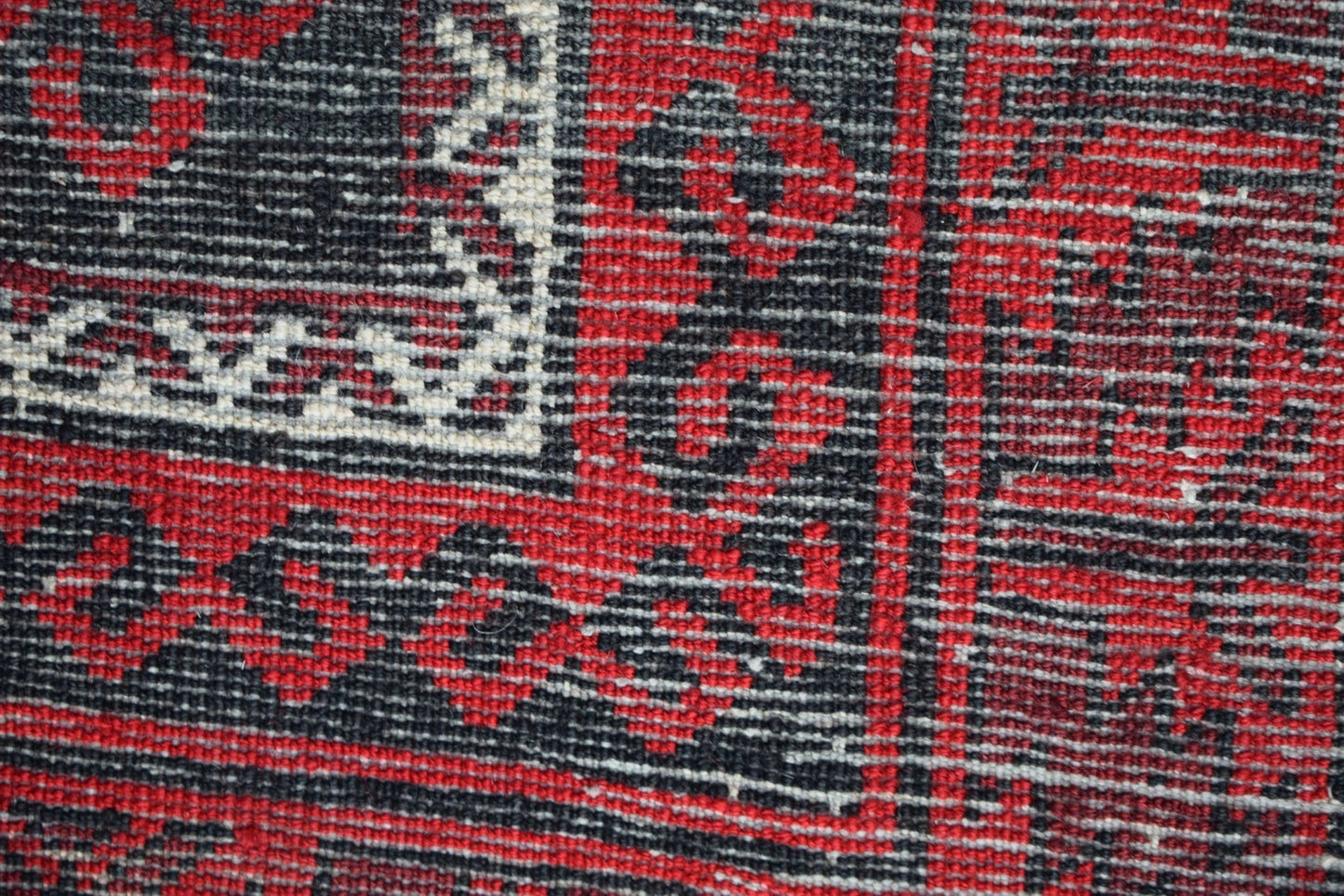 A close-up of a vintage Afghan Baluch rug featuring a geometric pattern in red, black, and white.