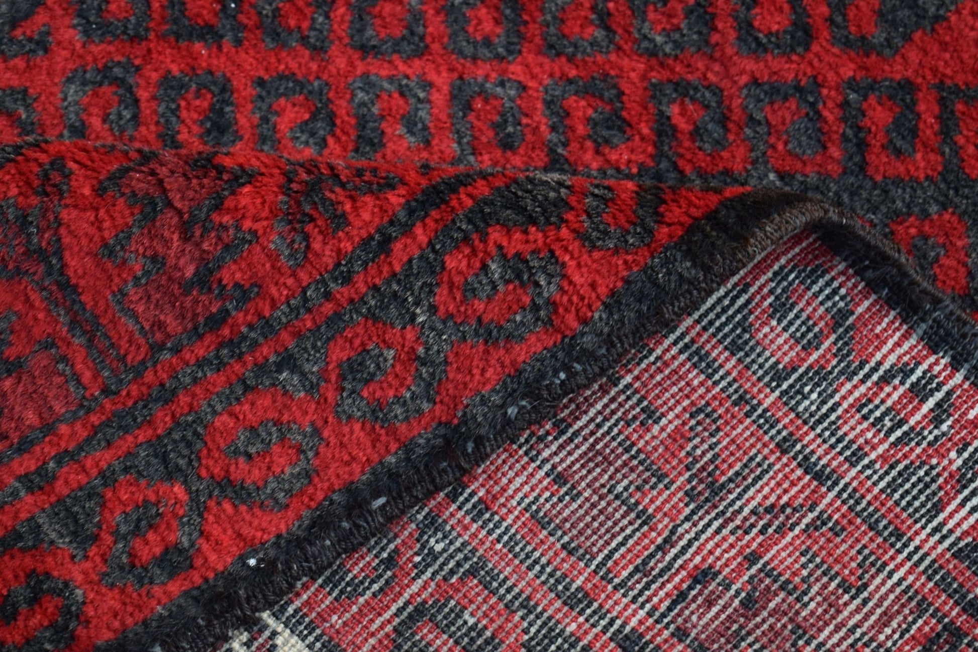 A vintage handmade Afghan Baluch rug featuring a red and black geometric pattern.