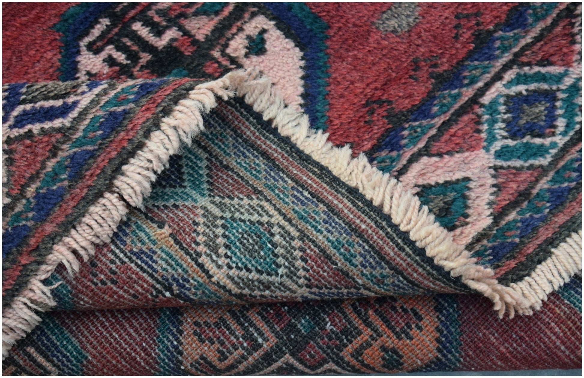 A vintage handmade Afghan Baluch wool rug with a folded corner showing its intricate tribal pattern.