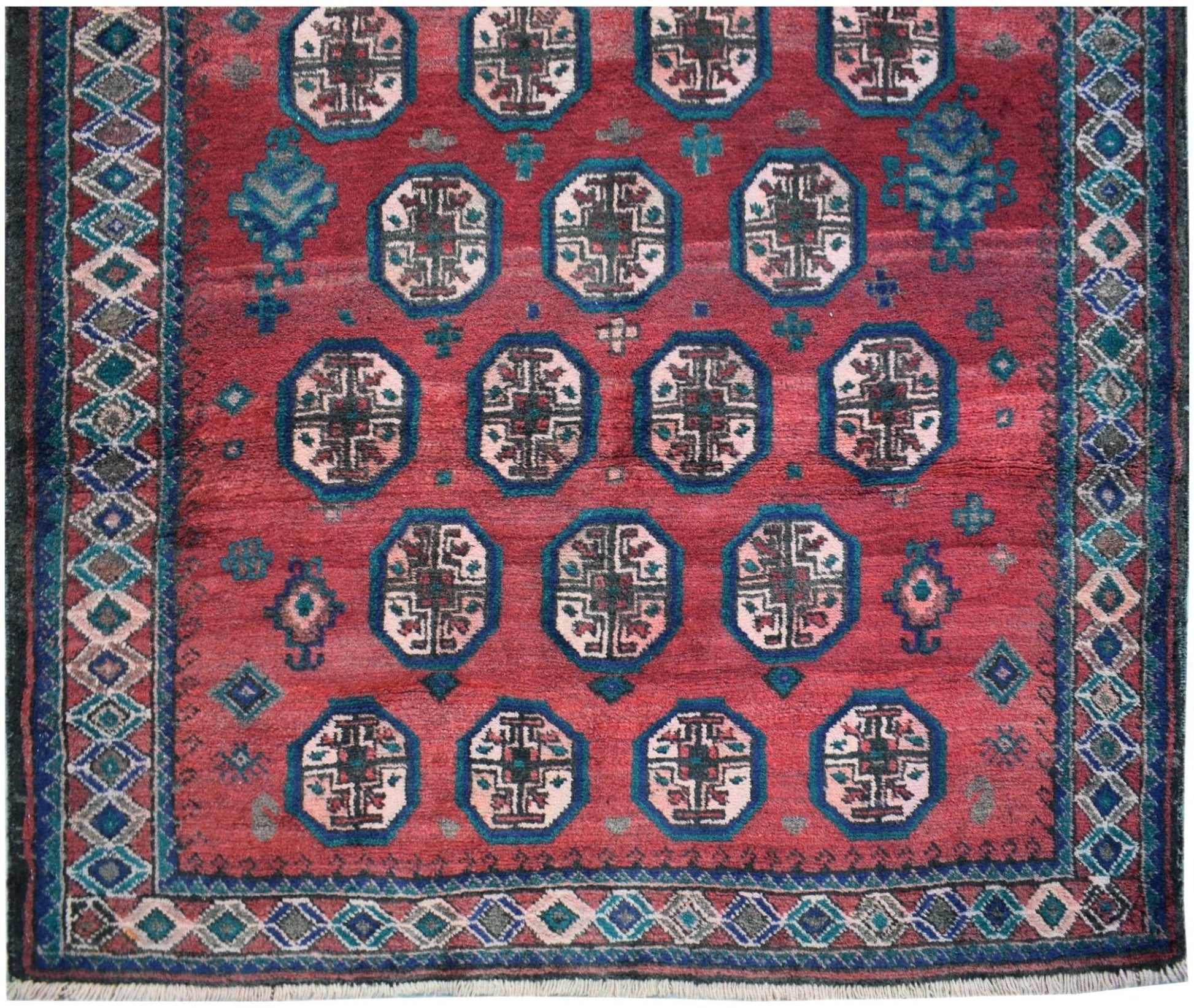 A vintage Afghan Baluch rug featuring repeating geometric motifs in red, blue, and cream tones.