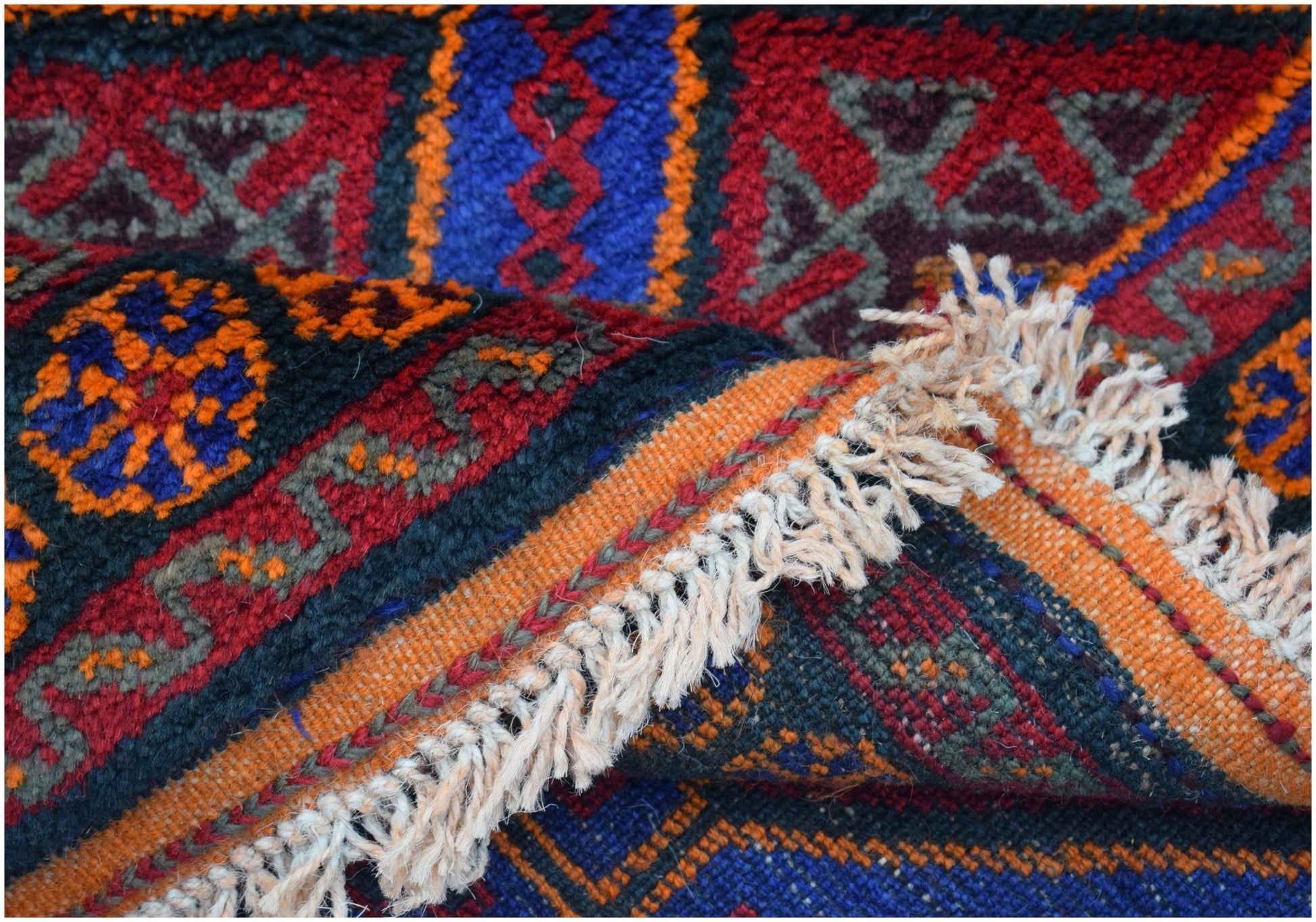 A vintage Afghan Baluch wool rug featuring intricate geometric patterns in red, blue, and orange.