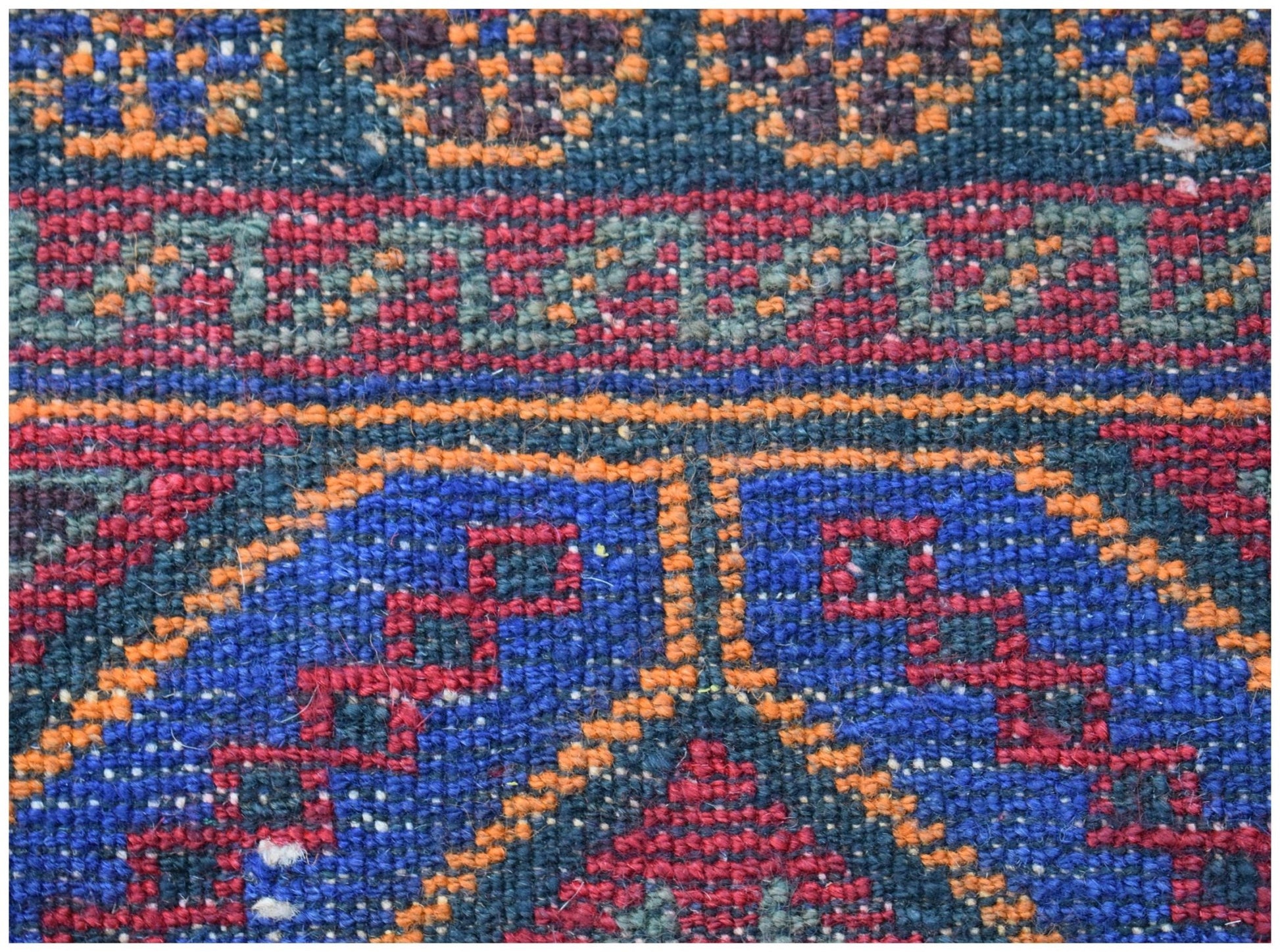 A close-up of a vintage Afghan Baluch wool rug featuring geometric patterns in blue, red, and orange.