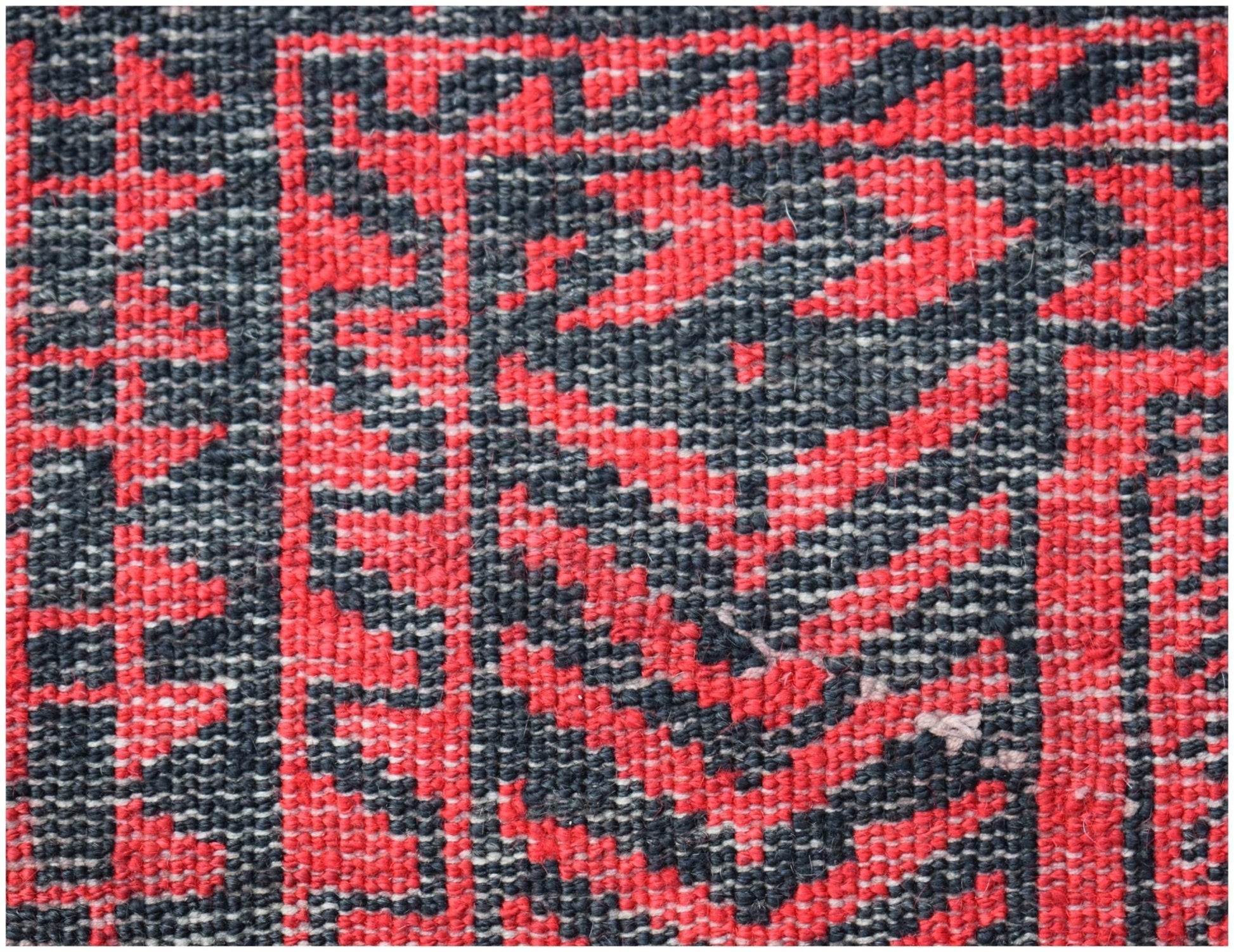 A close-up of a vintage Afghan Baluch rug featuring a geometric pattern in red and black wool.