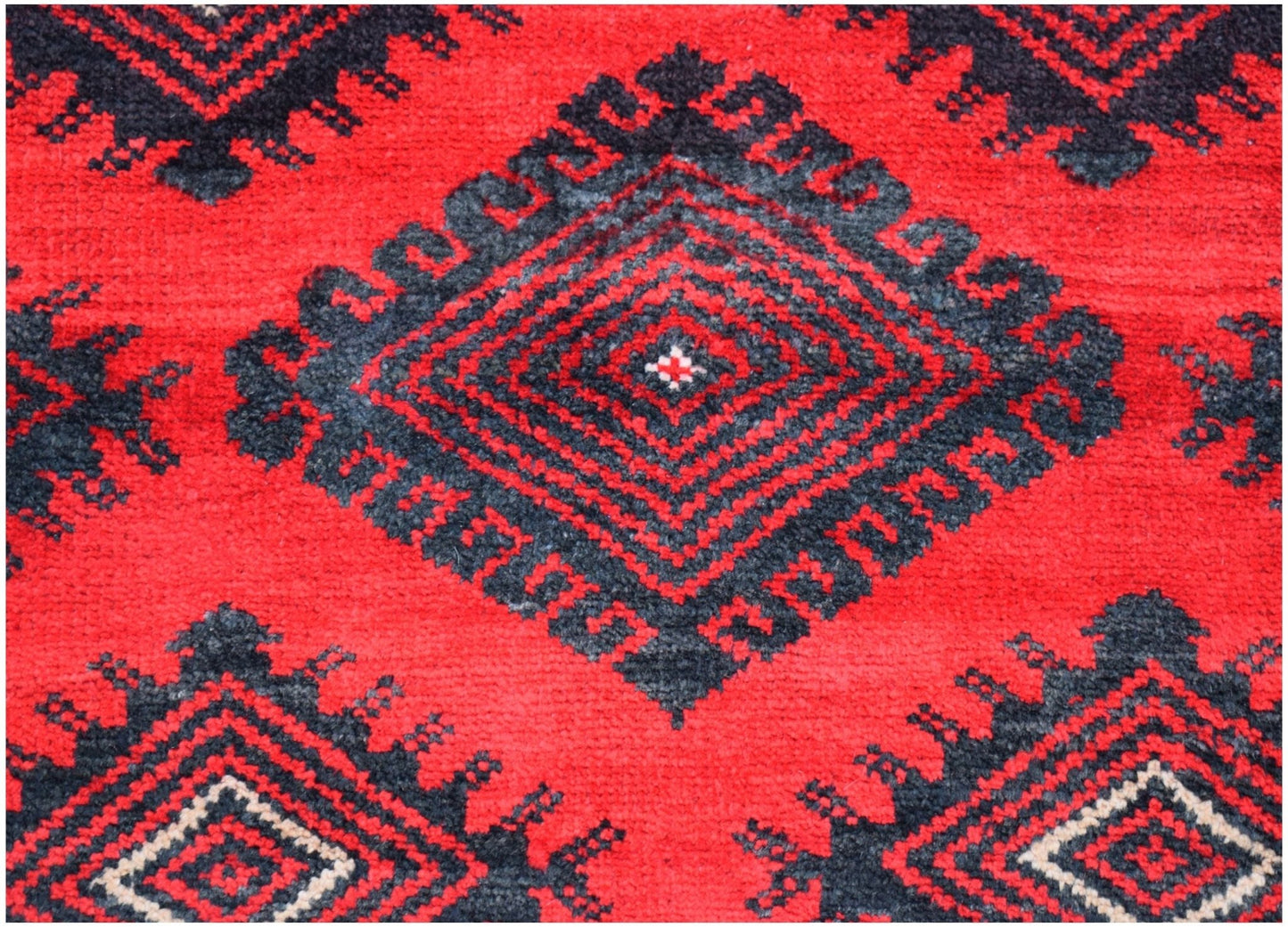 A vintage Afghan Baluch rug featuring a repeating black diamond pattern on a vibrant red background.