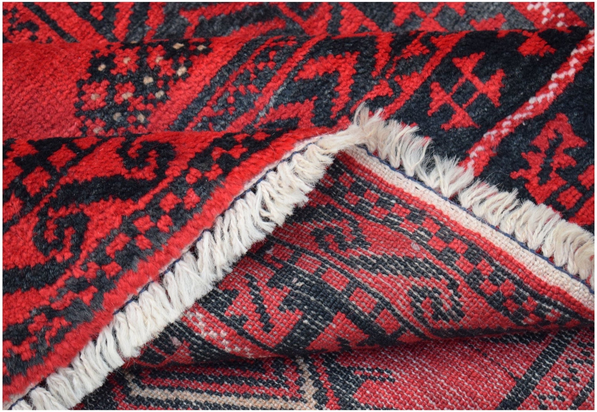 A folded vintage Afghan Baluch rug featuring a geometric red and black wool pattern.