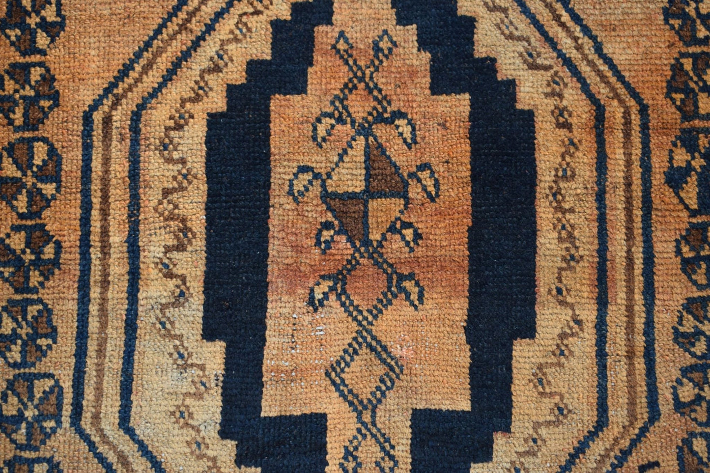 A vintage Afghan Baluch rug featuring a dark blue geometric medallion on a textured orange field.