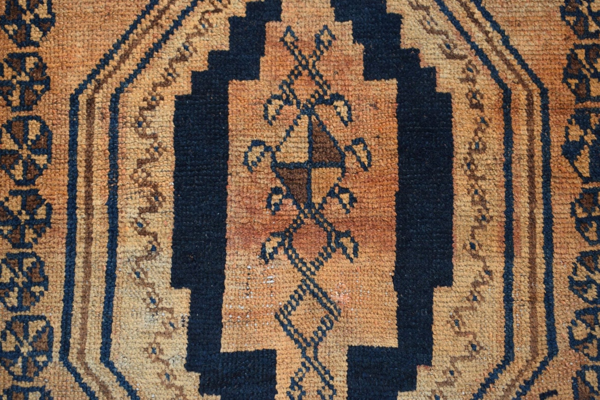 A vintage Afghan Baluch rug featuring a dark blue geometric medallion on a textured orange field.