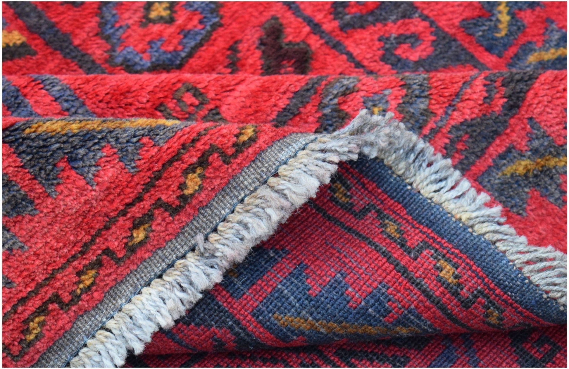 A vintage handmade Afghan Baluch wool rug featuring a geometric pattern in red and dark blue.