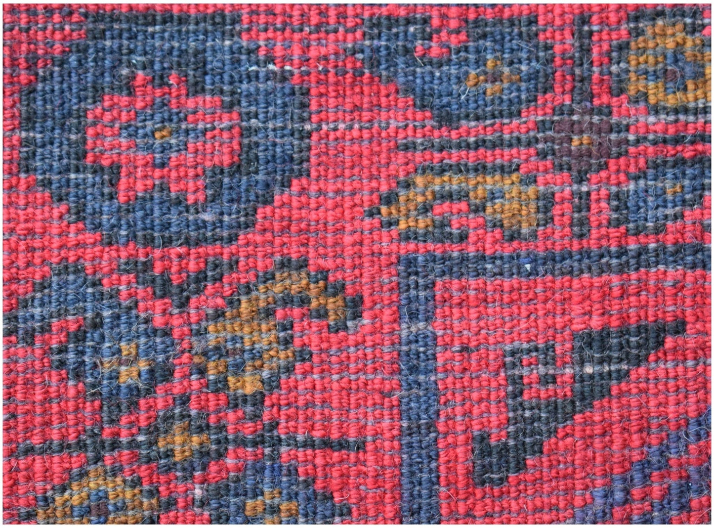 A close-up of a vintage Afghan Baluch rug featuring a geometric floral pattern in red and blue.