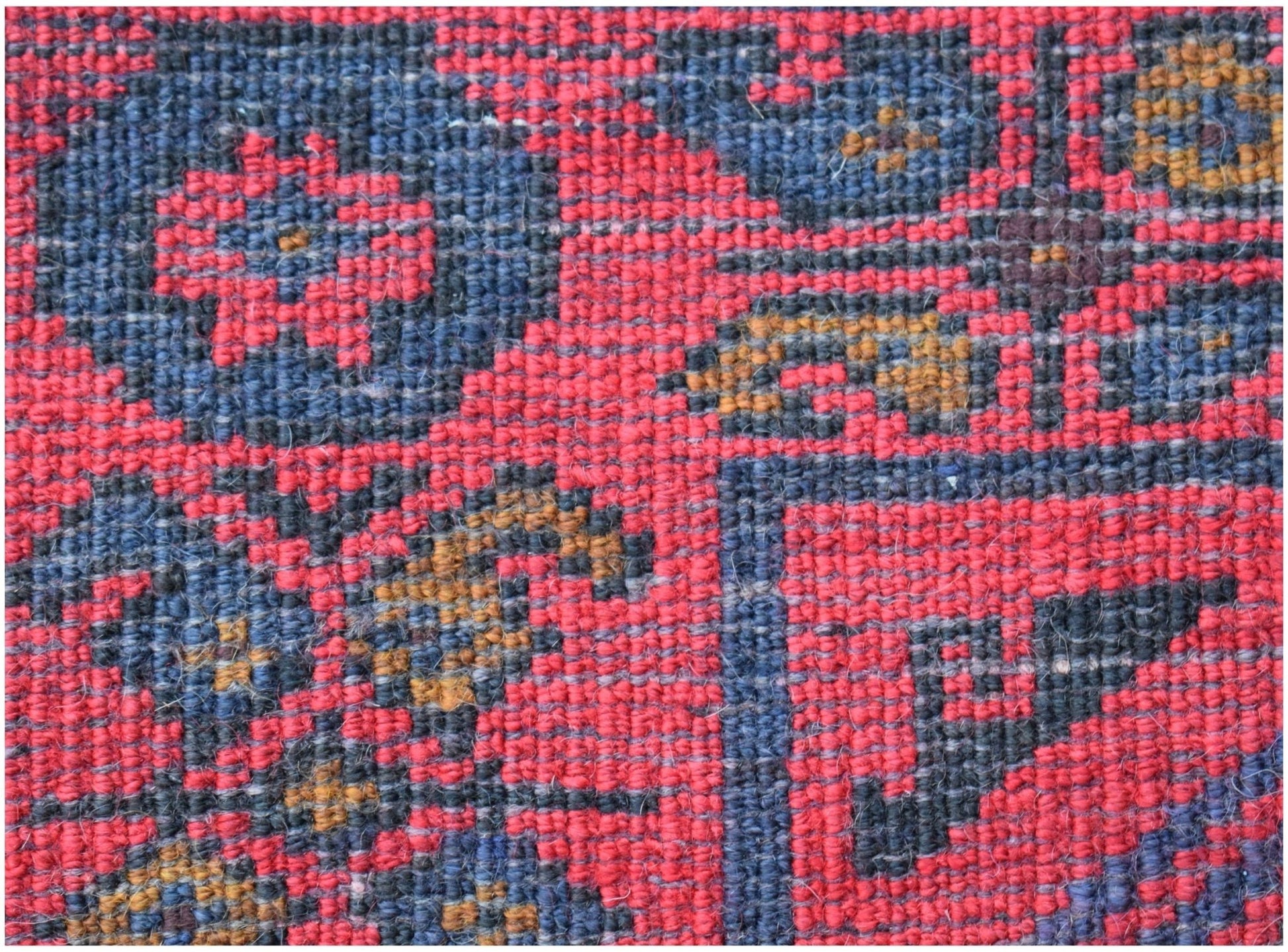 A close-up of a vintage Afghan Baluch rug featuring a geometric floral pattern in red and blue.