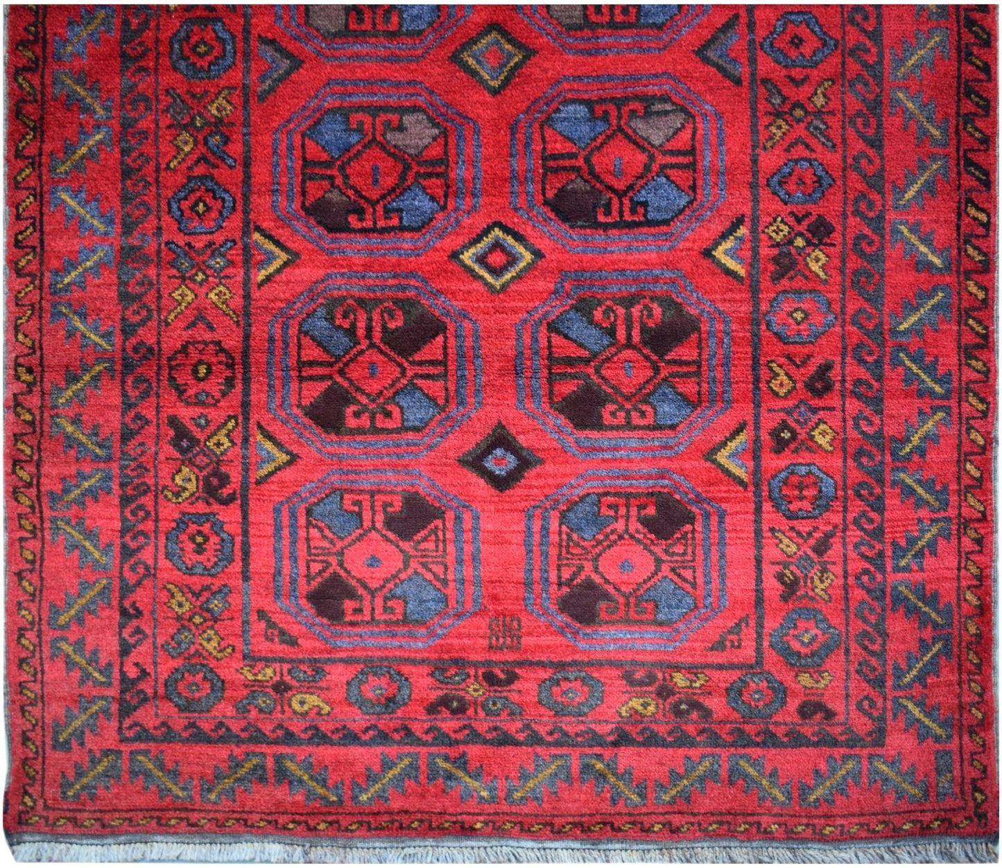 A vintage Afghan Baluch rug featuring geometric octagonal motifs in red, blue, and dark tones.