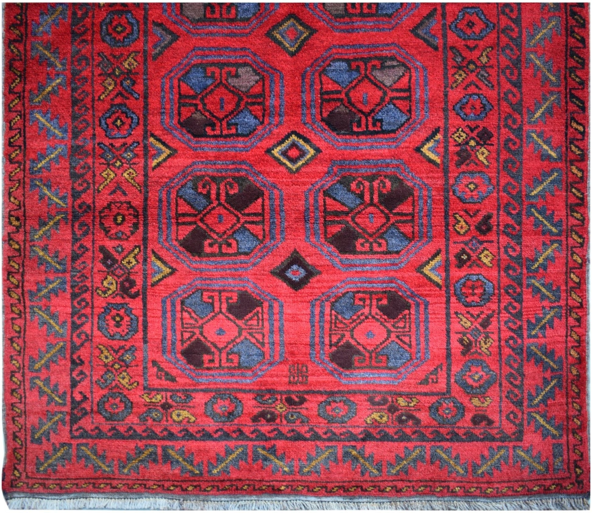 A vintage Afghan Baluch rug featuring geometric octagonal motifs in red, blue, and dark tones.
