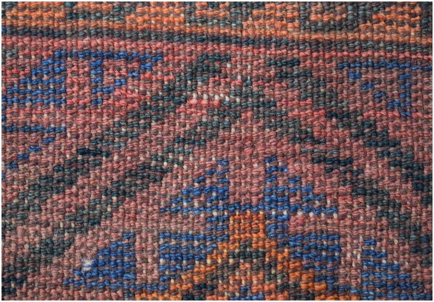 A close-up view of a vintage Afghan Baluch rug featuring a geometric pattern in red, blue, and orange.