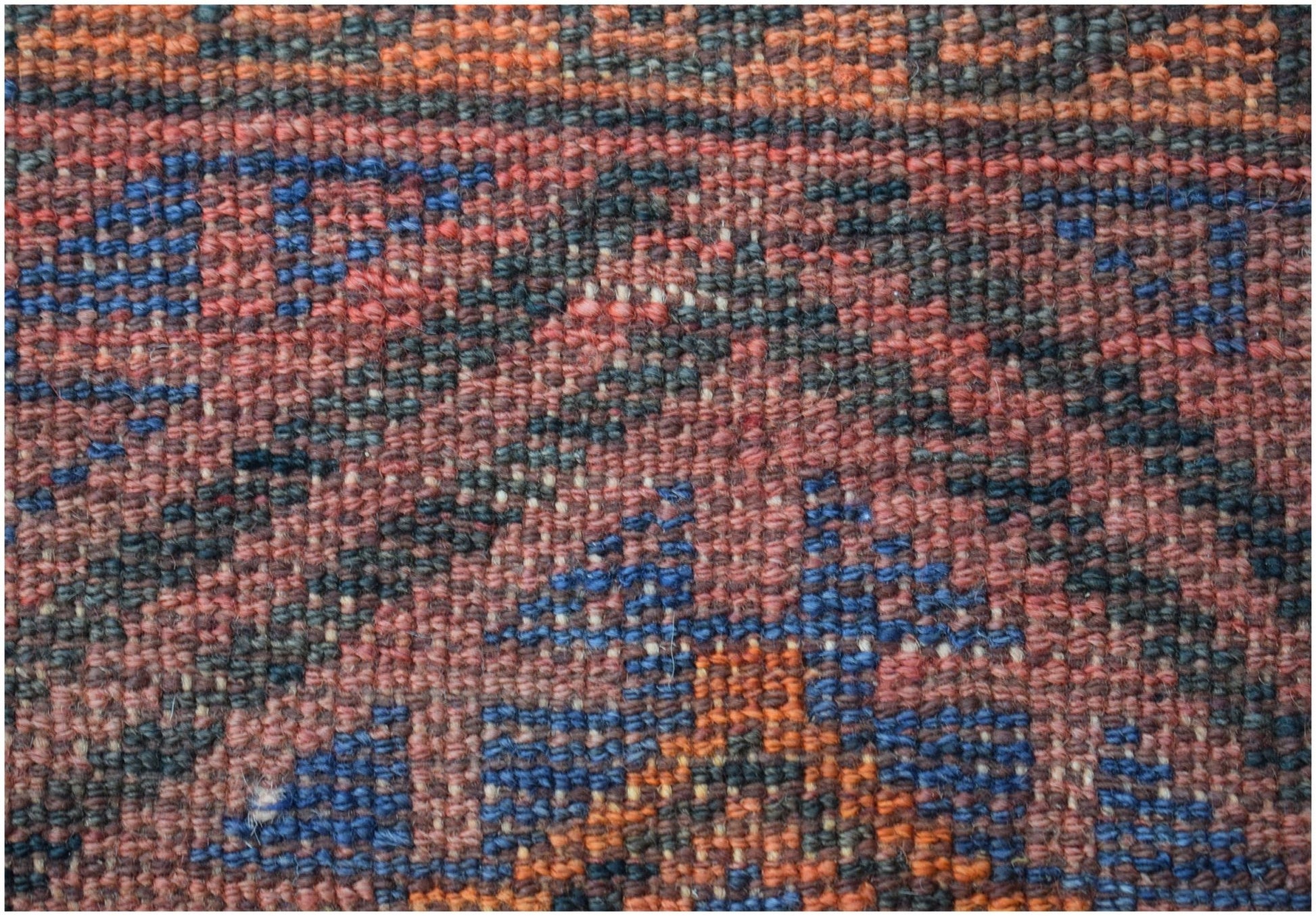 A close-up view of a vintage Afghan Baluch rug featuring a geometric pattern in red, blue, and orange.