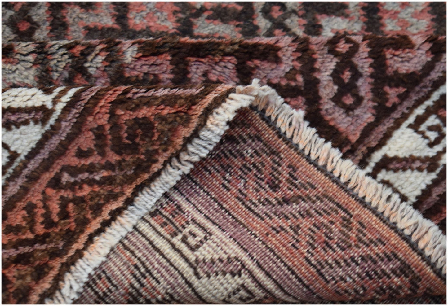 A close-up view of a vintage Afghan Baluch rug showing its thick wool pile and woven underside.