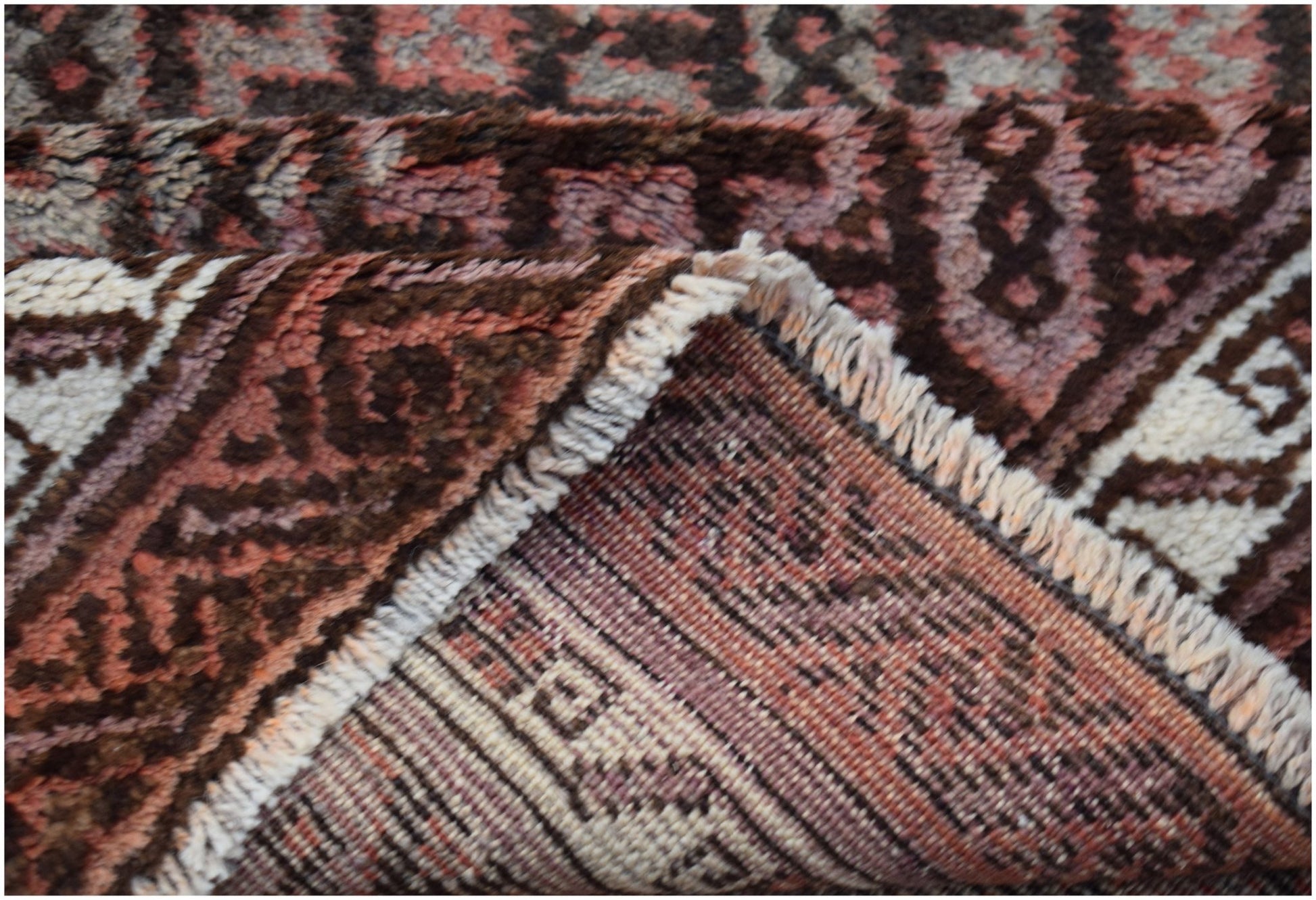 A close-up view of a vintage Afghan Baluch rug showing its thick wool pile and woven underside.