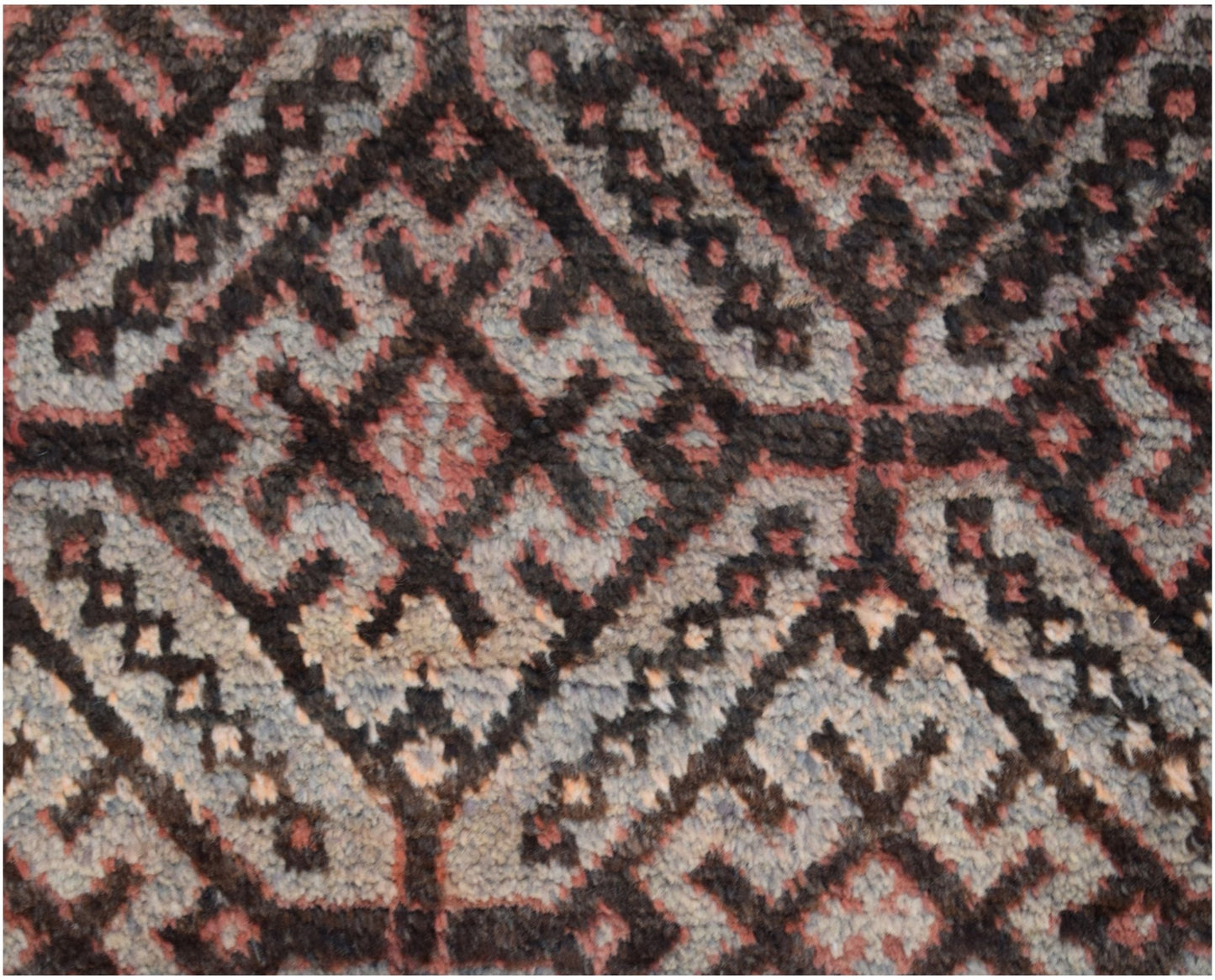 A close-up of a vintage Afghan Baluch wool rug featuring a geometric diamond pattern in dark tones.