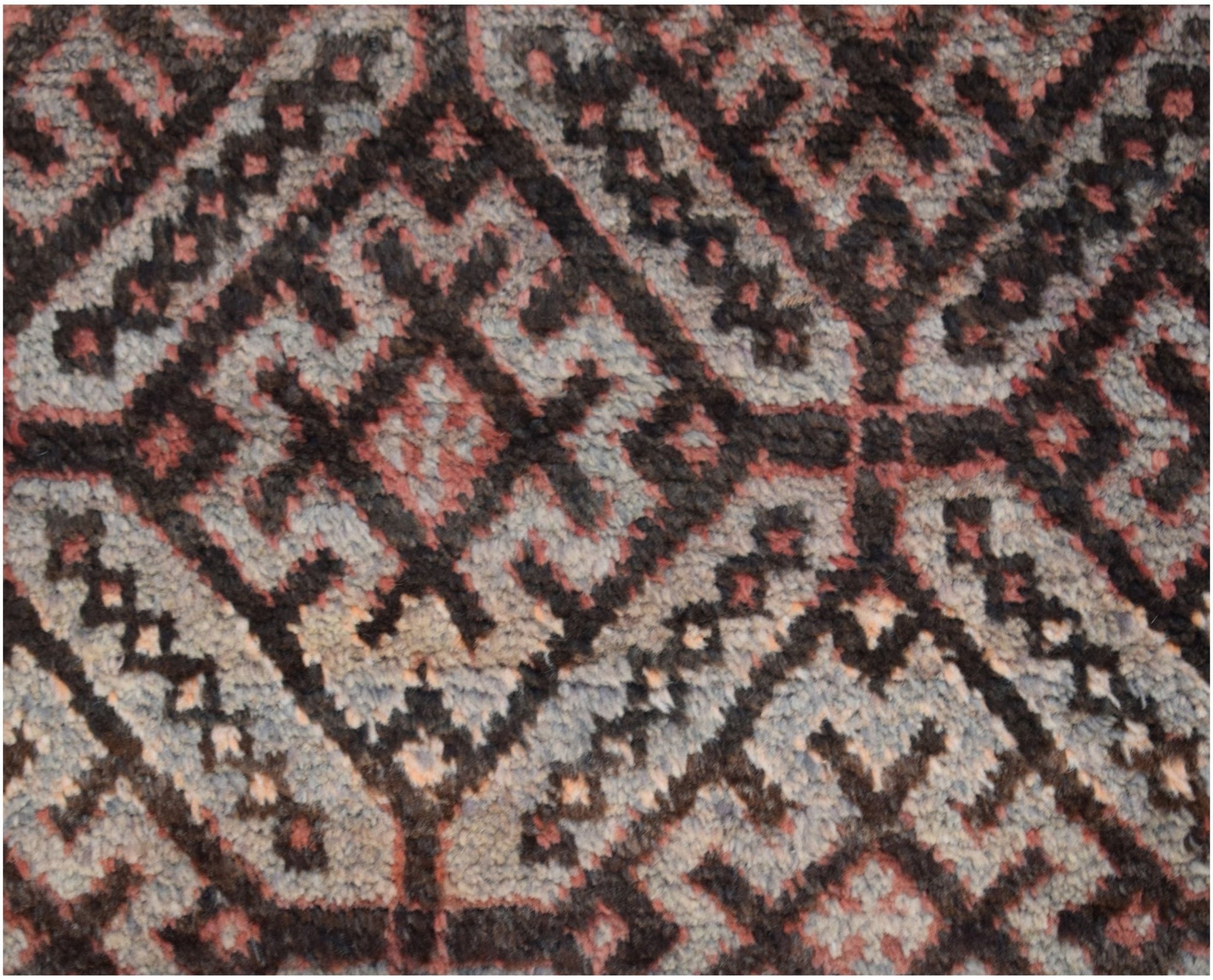 A close-up of a vintage Afghan Baluch wool rug featuring a geometric diamond pattern in dark tones.