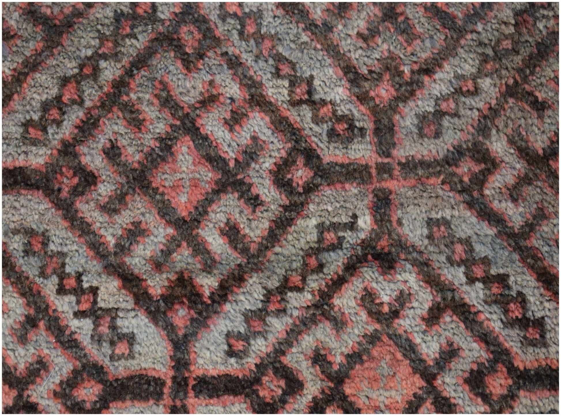 A close-up of a vintage Afghan Baluch rug featuring a geometric pattern in red, brown, and grey.