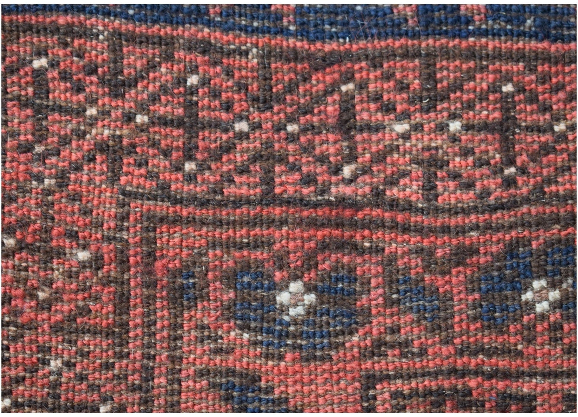 A close-up of a vintage Afghan Baluch wool rug featuring geometric patterns in red, blue, and brown.