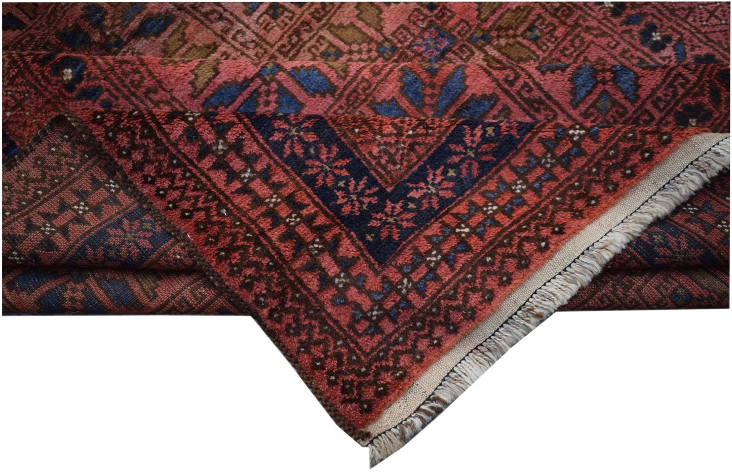 A vintage Afghan Baluch rug with a folded corner showing geometric patterns in red and blue.