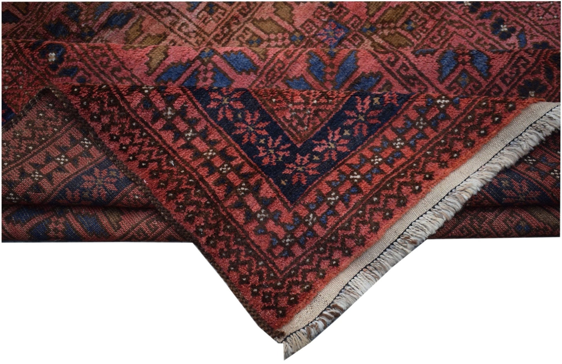 A vintage Afghan Baluch rug with a folded corner showing geometric patterns in red and blue.