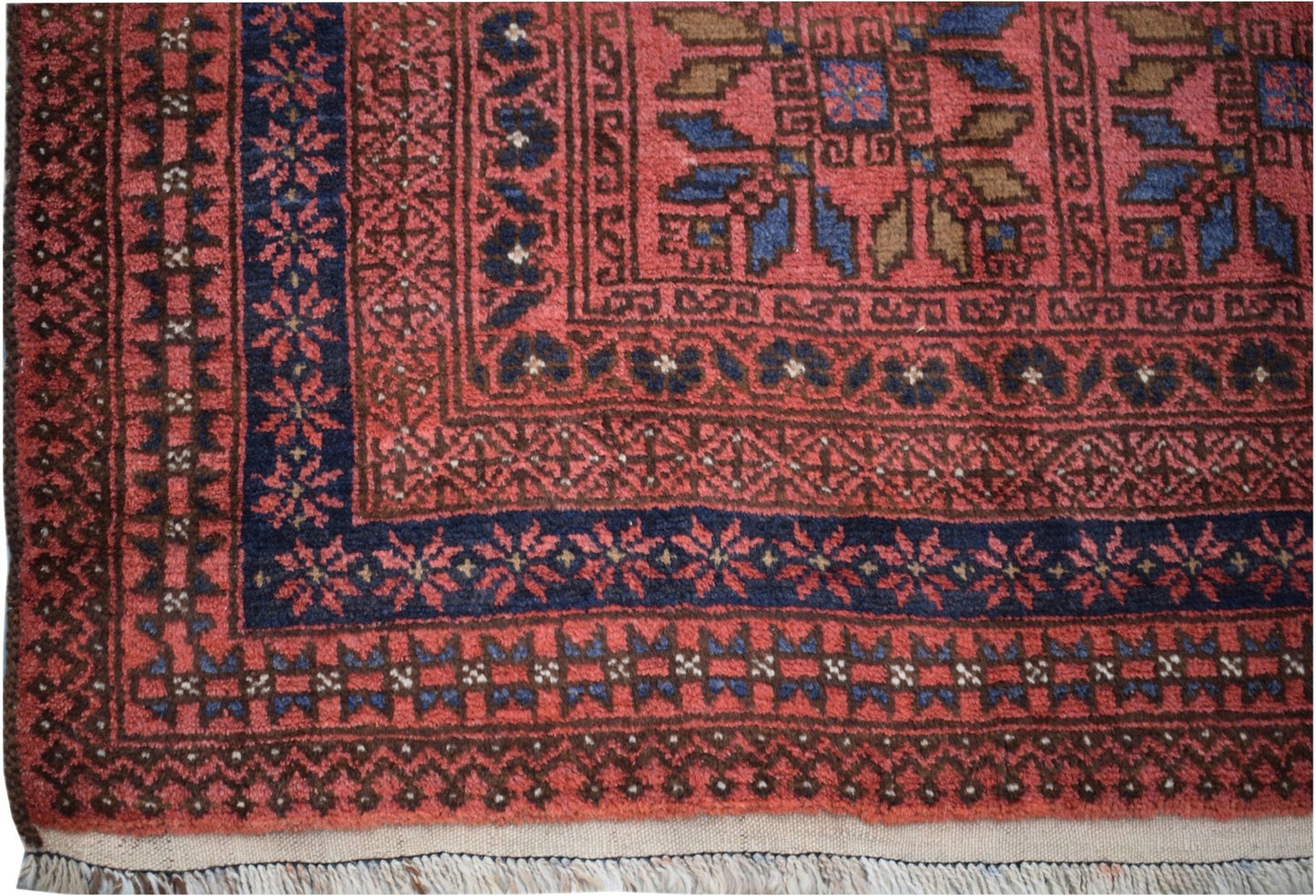 A vintage Afghan Baluch rug featuring a geometric pattern in red, blue, and brown wool.