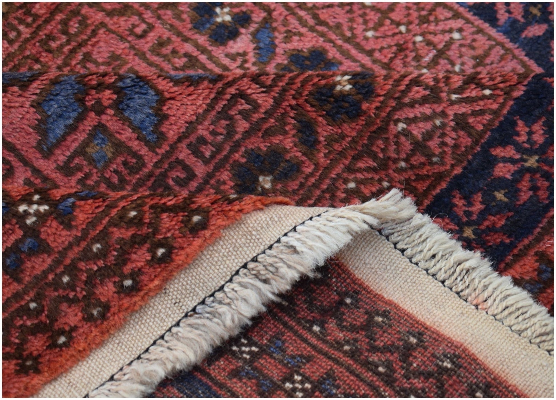 A close-up of a vintage Afghan Baluch rug showing its red and blue geometric wool pile and fringe.