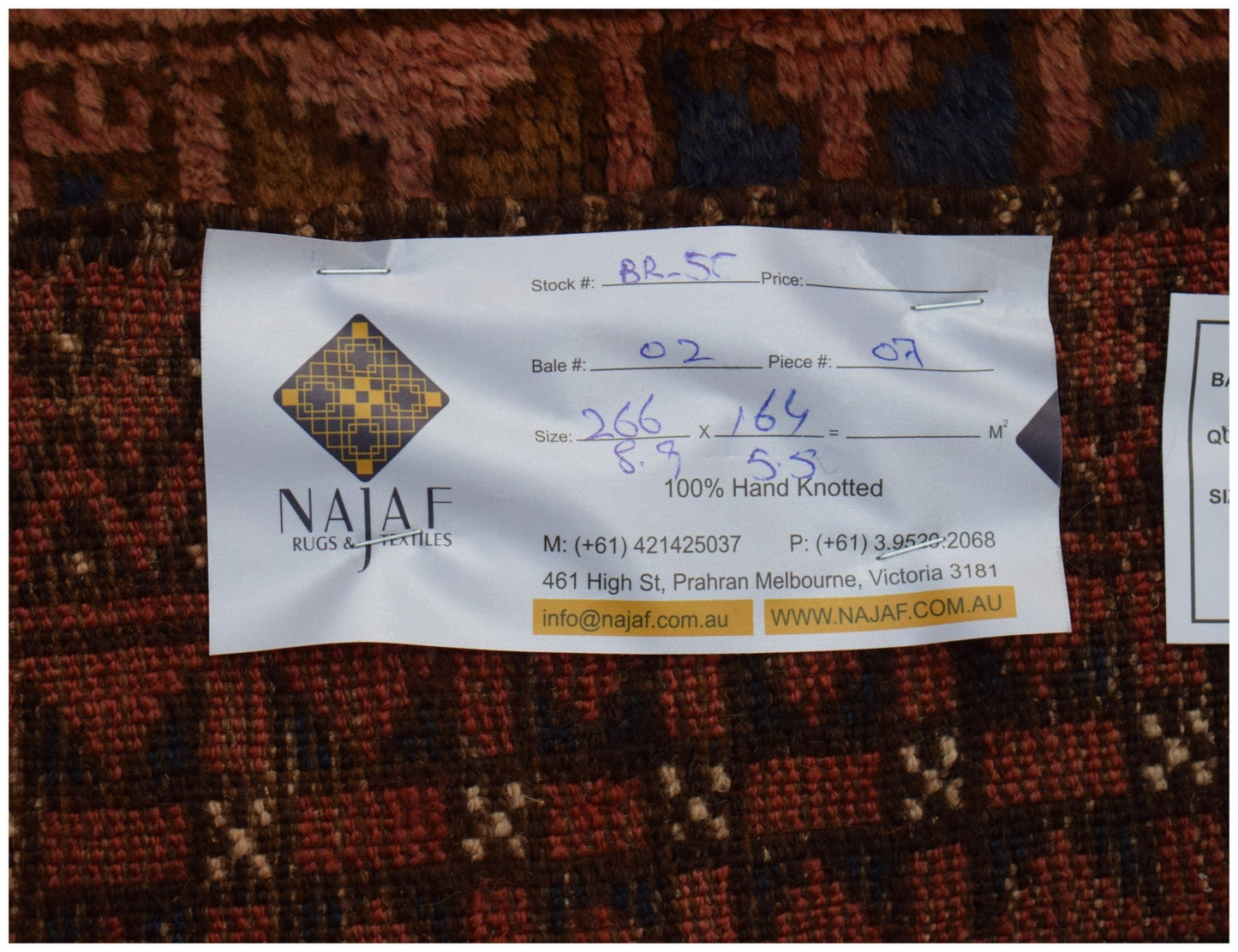 A vintage Afghan Baluch rug with a geometric pattern and a product tag attached.