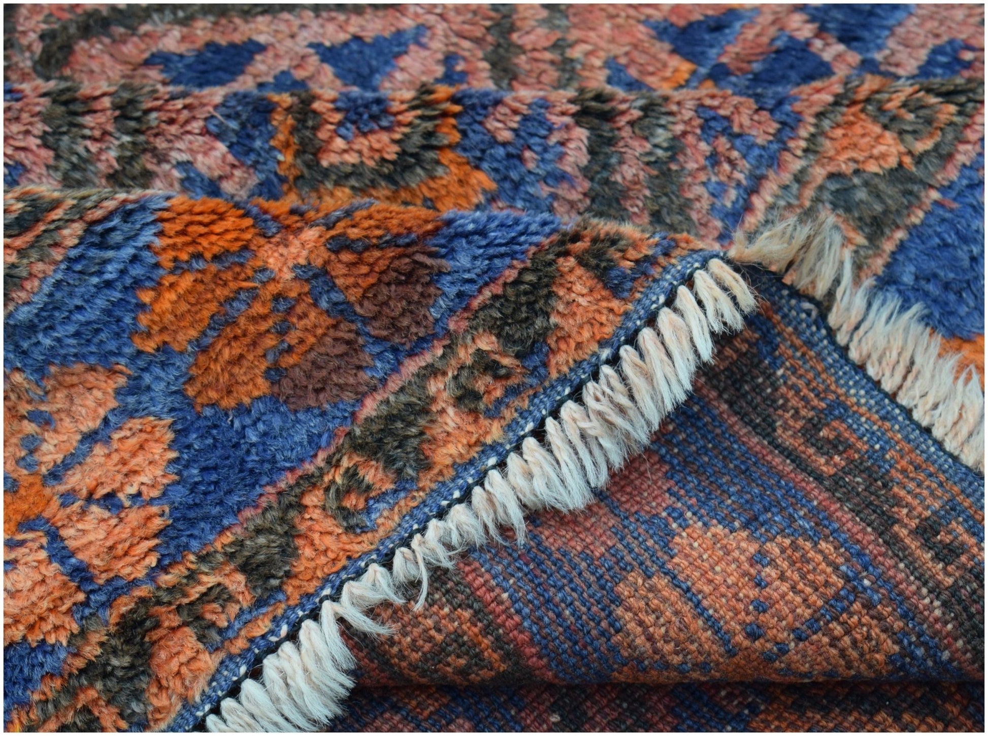 A close-up view of a vintage Afghan Baluch rug showing its thick wool pile and woven underside.