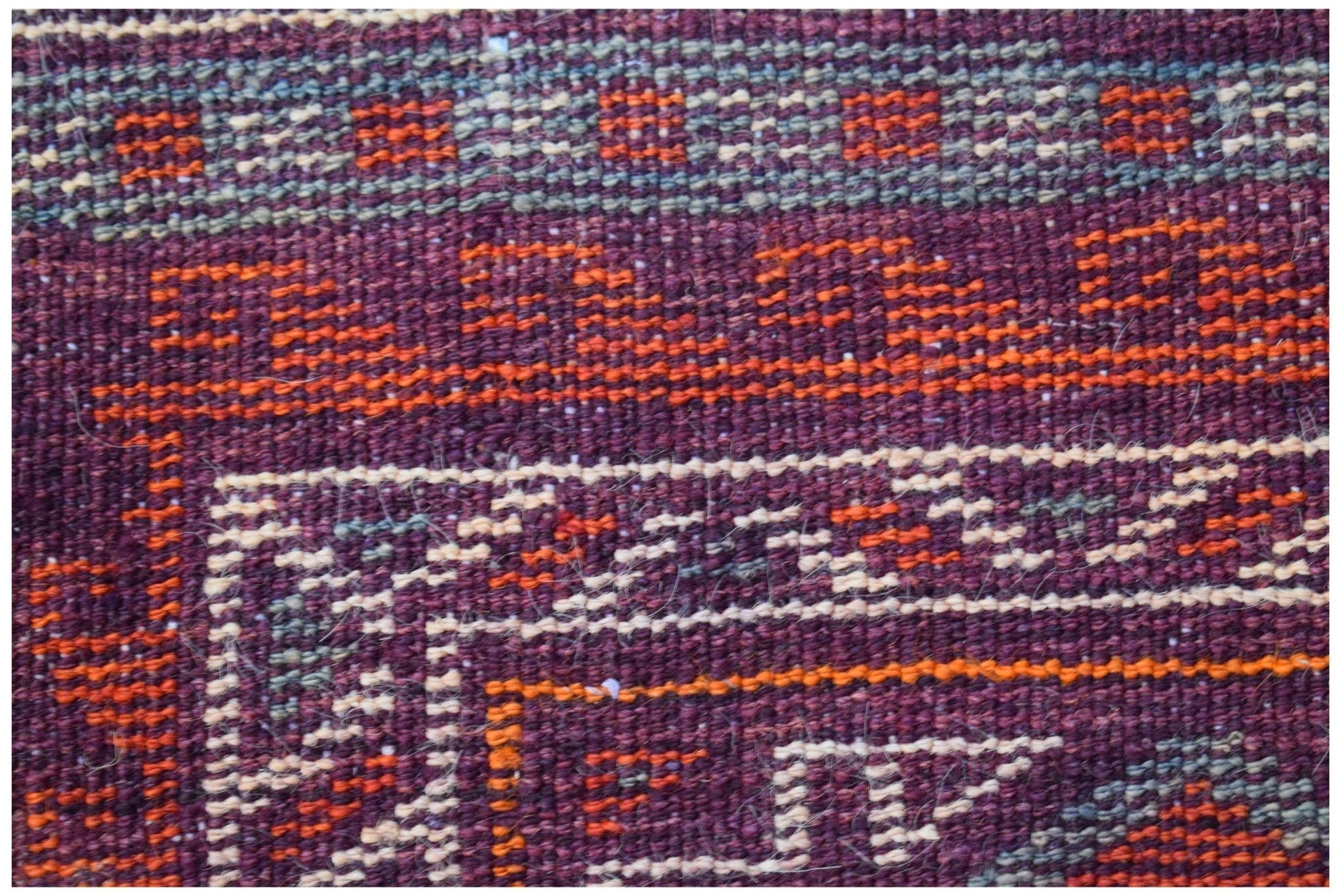 A close-up of a vintage Afghan Baluch rug featuring geometric patterns in deep red and orange wool.