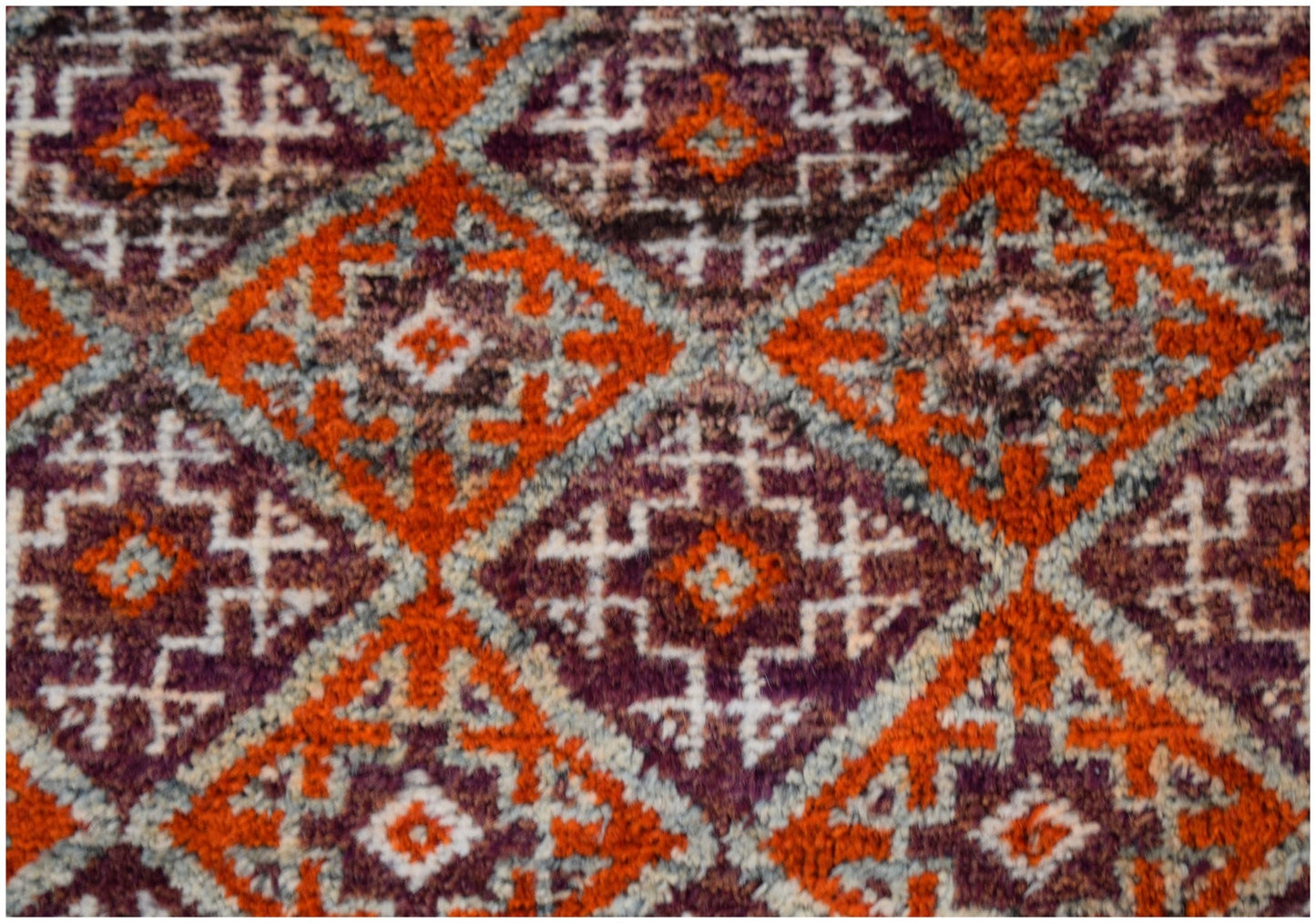 A vintage Afghan Baluch rug featuring a repeating diamond pattern in orange, purple, and white.