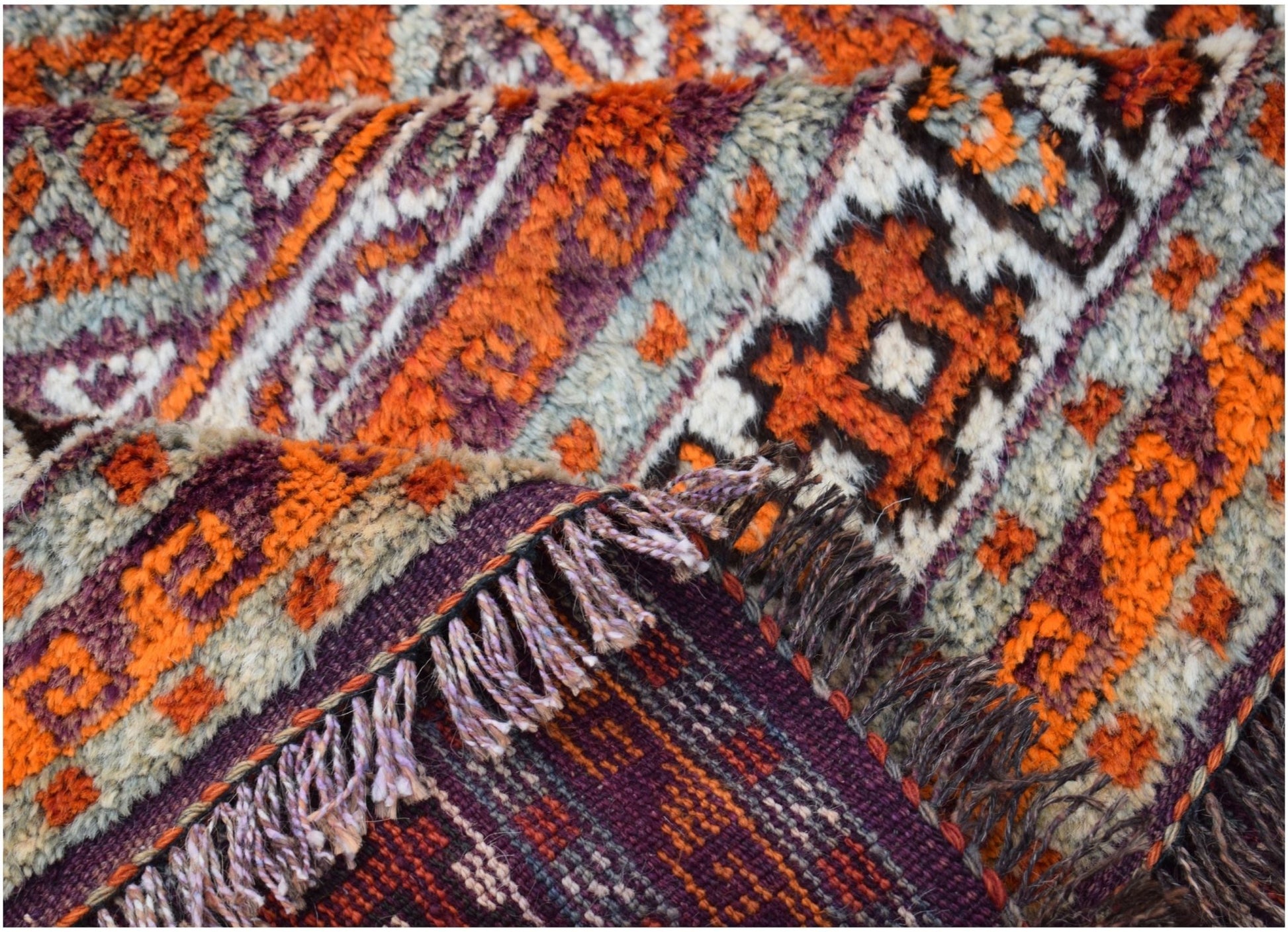 A vintage Afghan Baluch rug featuring a geometric pattern in orange, purple, and cream wool.