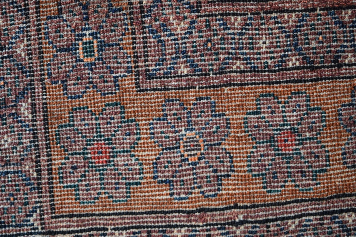 A close-up of a vintage Afghan Baluch rug featuring geometric floral patterns in earthy tones.