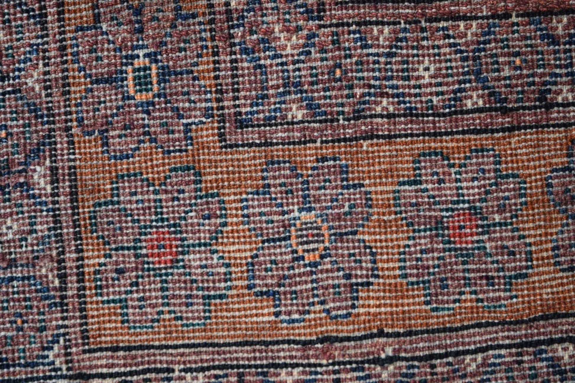 A close-up of a vintage Afghan Baluch rug featuring geometric floral patterns in earthy tones.