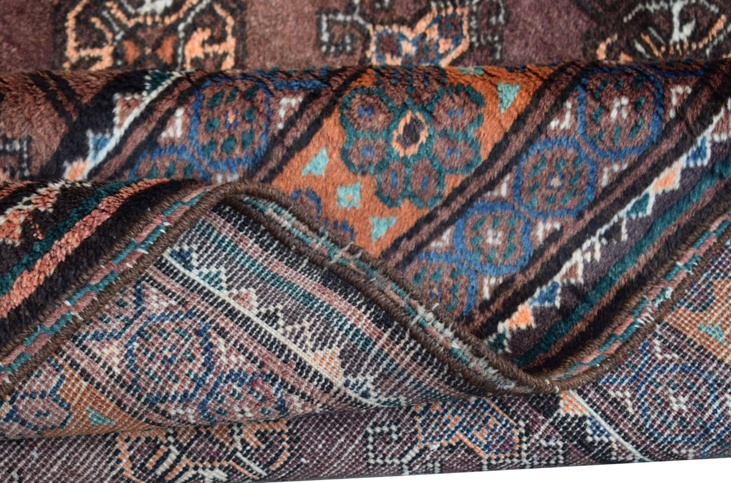 A folded vintage Afghan Baluch wool rug featuring intricate geometric patterns in earthy tones.