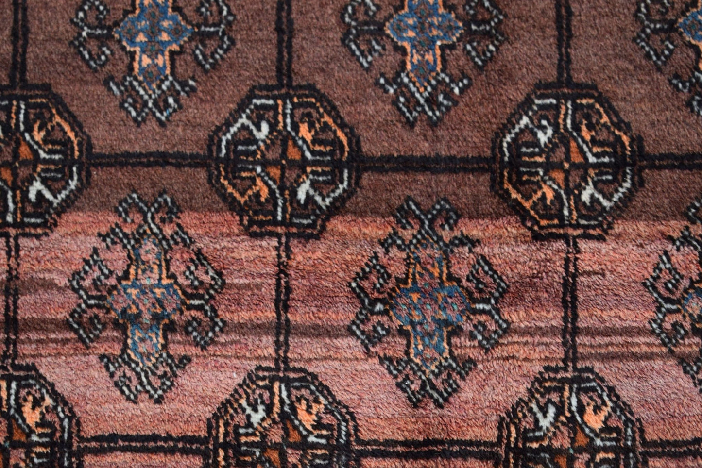 A vintage Afghan Baluch rug featuring a repeating geometric pattern in brown and blue tones.